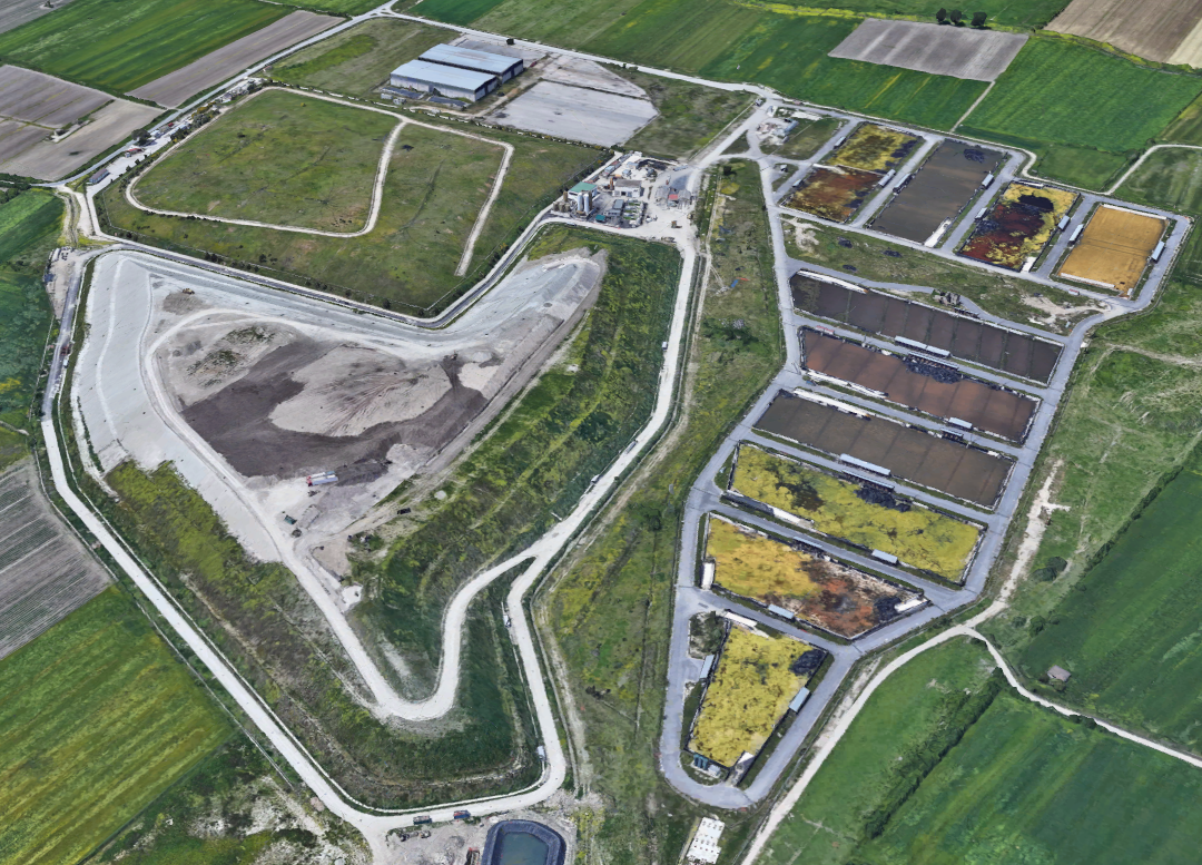 Immagine aerea di un complesso industriale con laghetti di trattamento delle acque e aree di stoccaggio, circondato da campi agricoli.