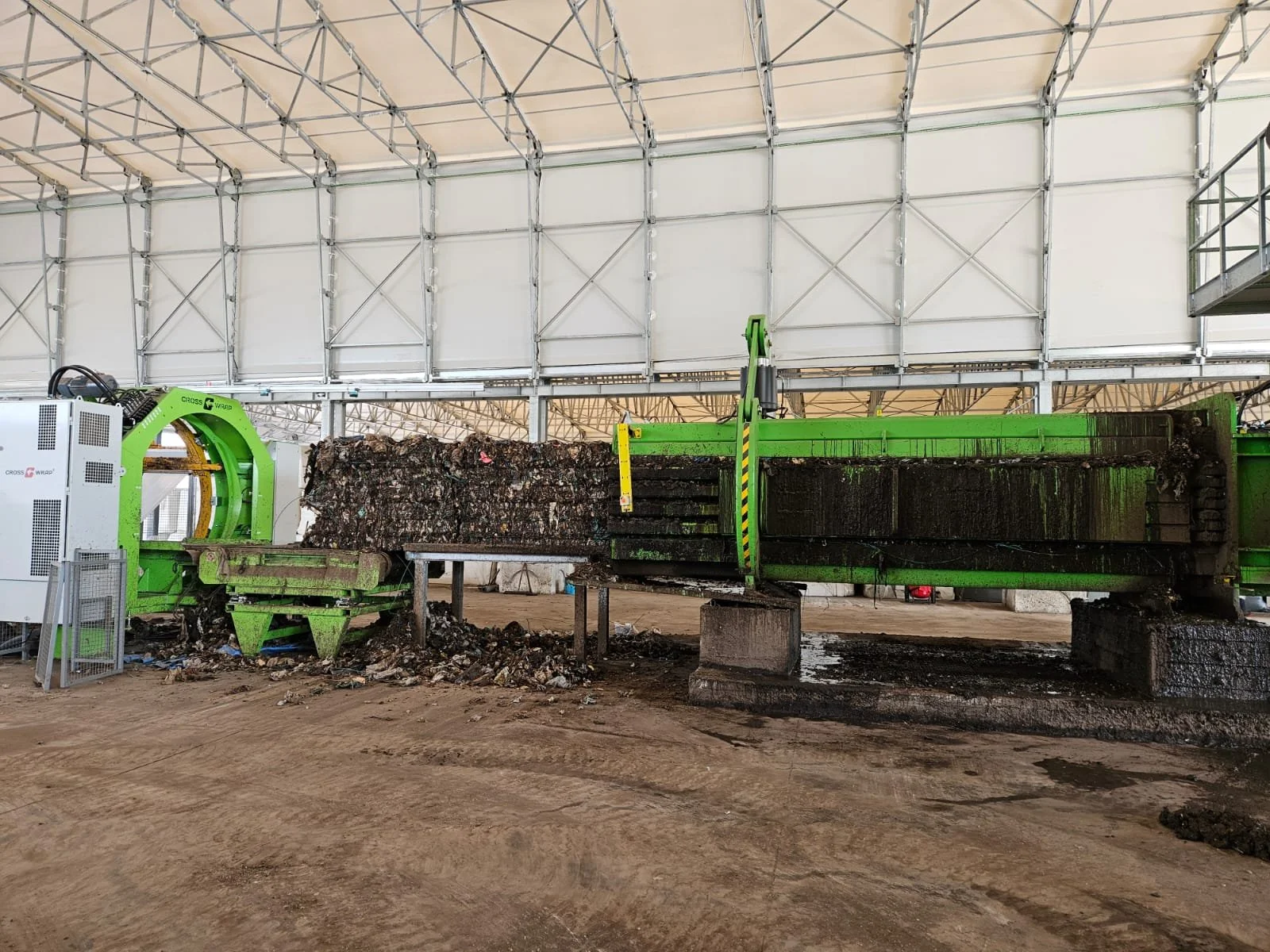 Una grande macchina di compostaggio con parti verdi, situata all’interno di una struttura coperta, che sta processando rifiuti organici o materiali infiniti.