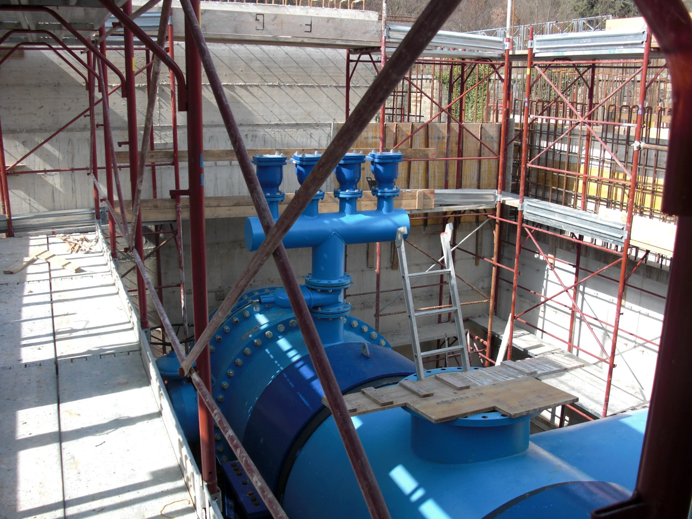 Immagine di un cantiere con impalcature rosse e una grande tubazione blu installata, con una scala di metallo appoggiata alla tubazione.