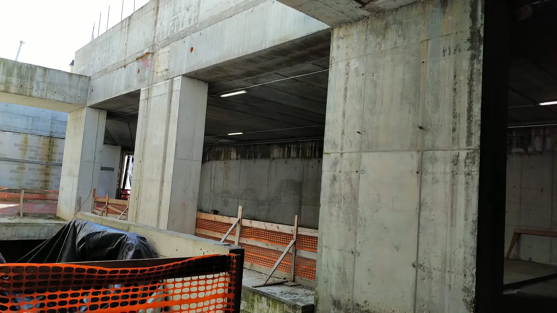 Struttura di cemento in costruzione con pannelli e barriere di sicurezza arancioni.
