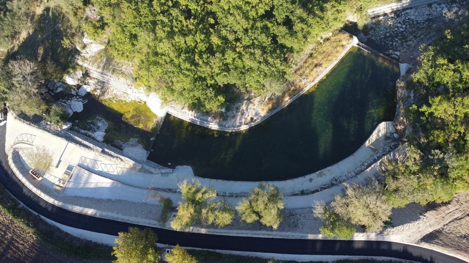 Veduta aerea di un parco naturale con un serbatoio di acqua circondato da alberi e sentieri, con un'area pavimentata lungo il perimetro.