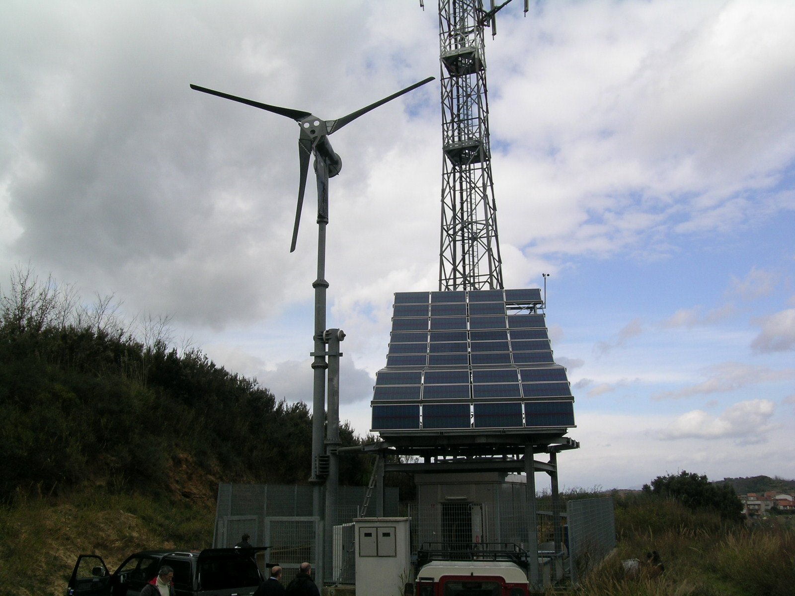 Pannello solare, wind turbine e torre di comunicazione in un'area aperta con nuvole nel cielo.