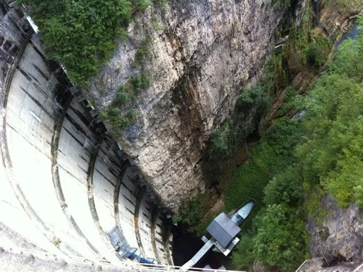 Una diga idroelettrica circondata da una vallata verde e una scogliera rocciosa.