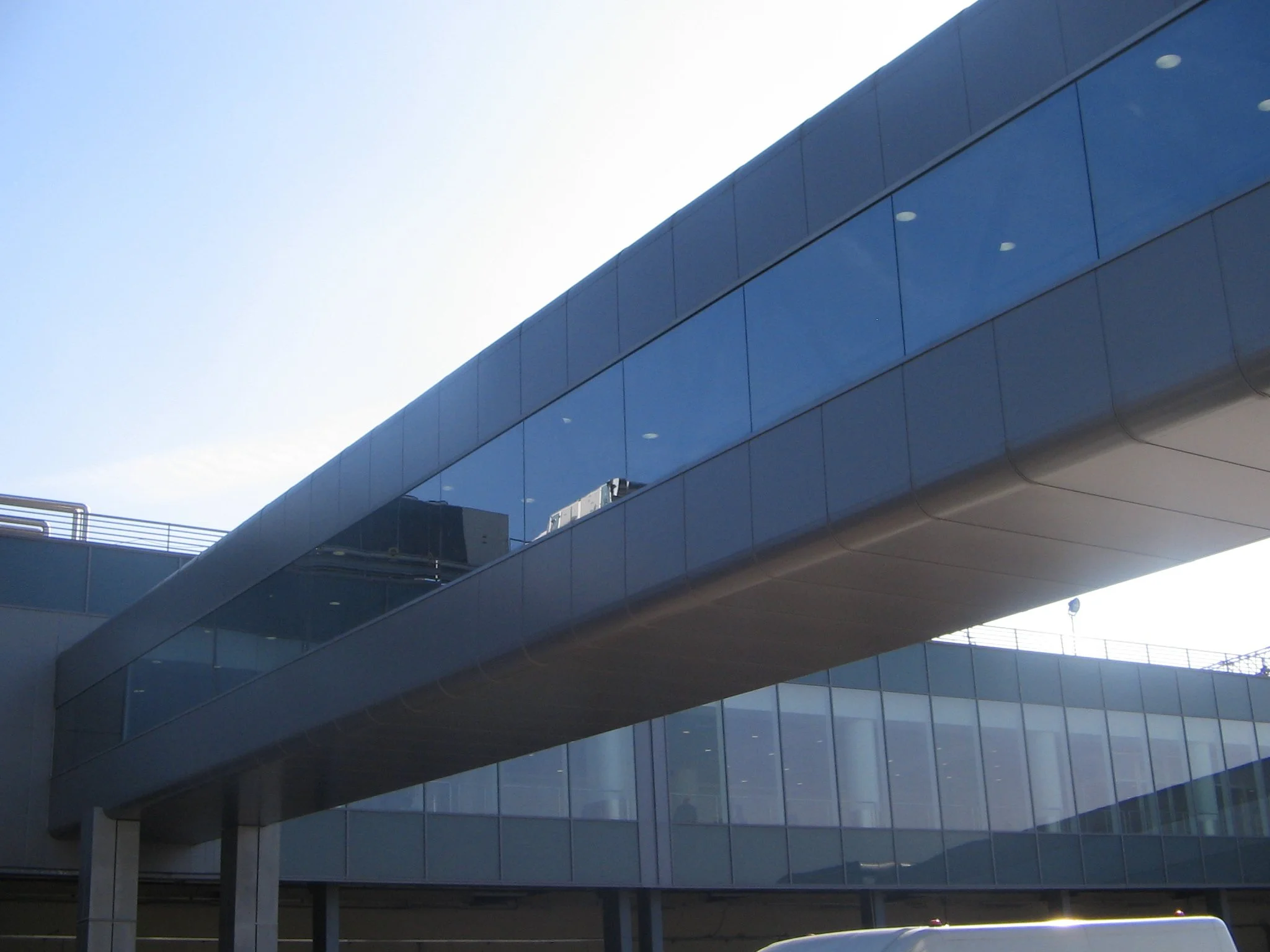 Edificio moderno con facciata in vetro blu riflettente, strutture sospese e illuminazione interna visibile tramite le finestre.