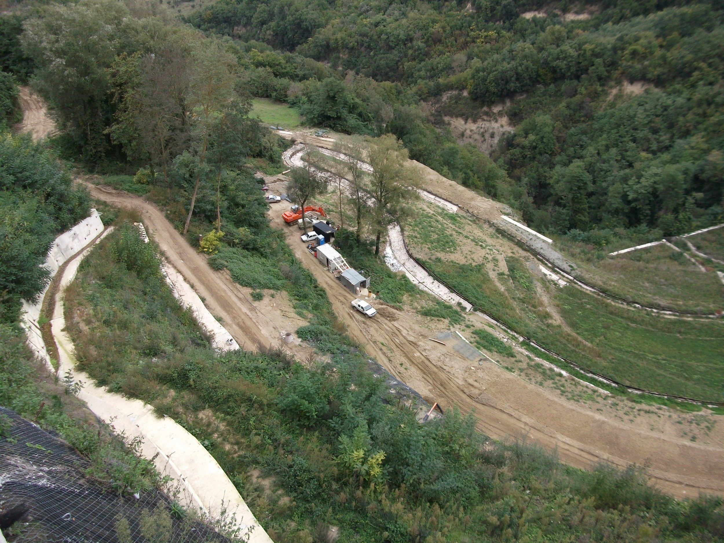 Un cantiere di costruzione su una collina, con veicoli come camion e attrezzature sparse lungo una strada di terra.