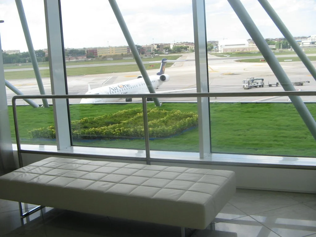 Interior dell'aeroporto con vista su un aereo in pista attraverso grandi finestrine vetrate