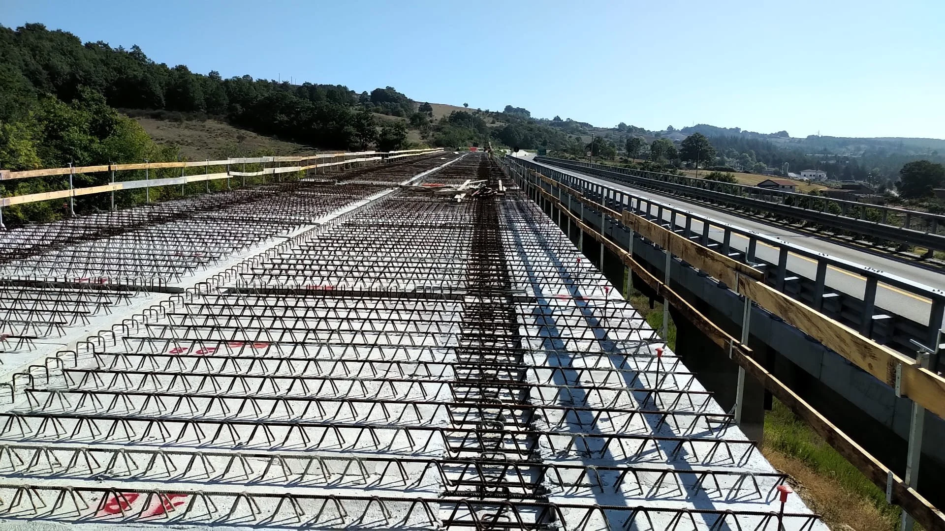 Strutture di rinforzo del ponte in costruzione, con strumenti e materiali di lavoro, in un'area rurale con colline e alberi sullo sfondo.