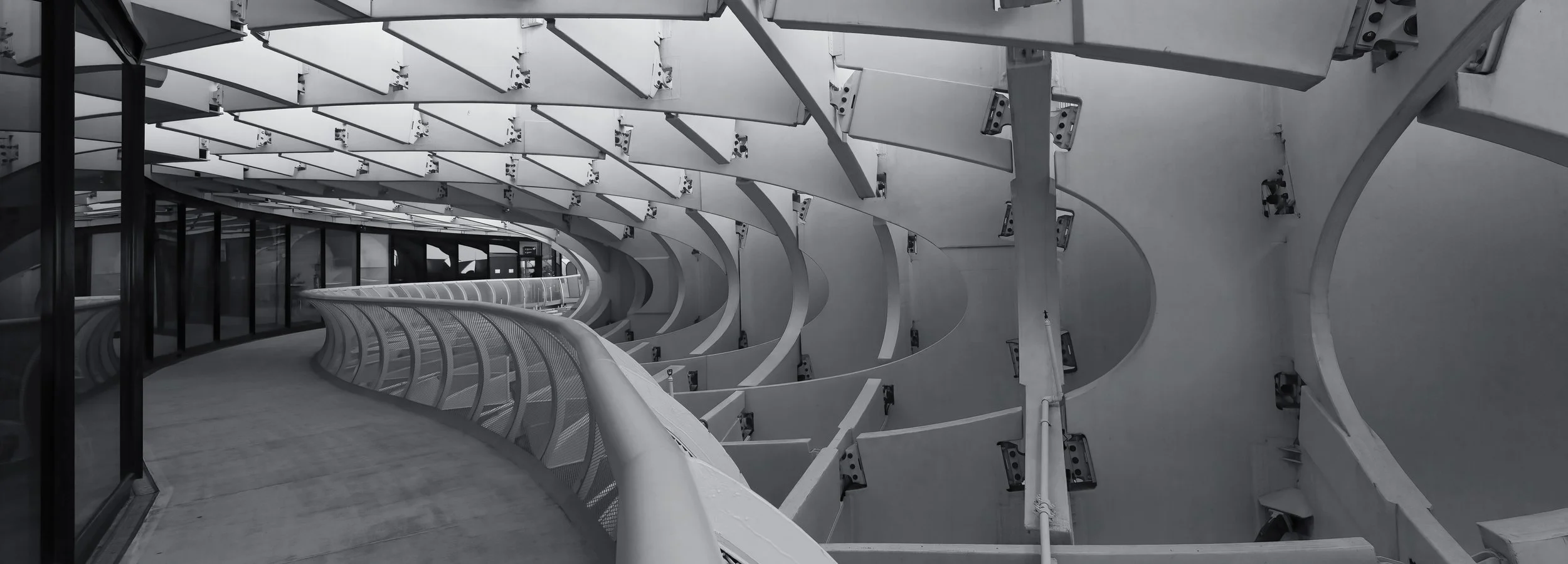 Interno di una struttura moderna in metallo e vetro con passaggio curvo e archi metallici, stile futuristico.