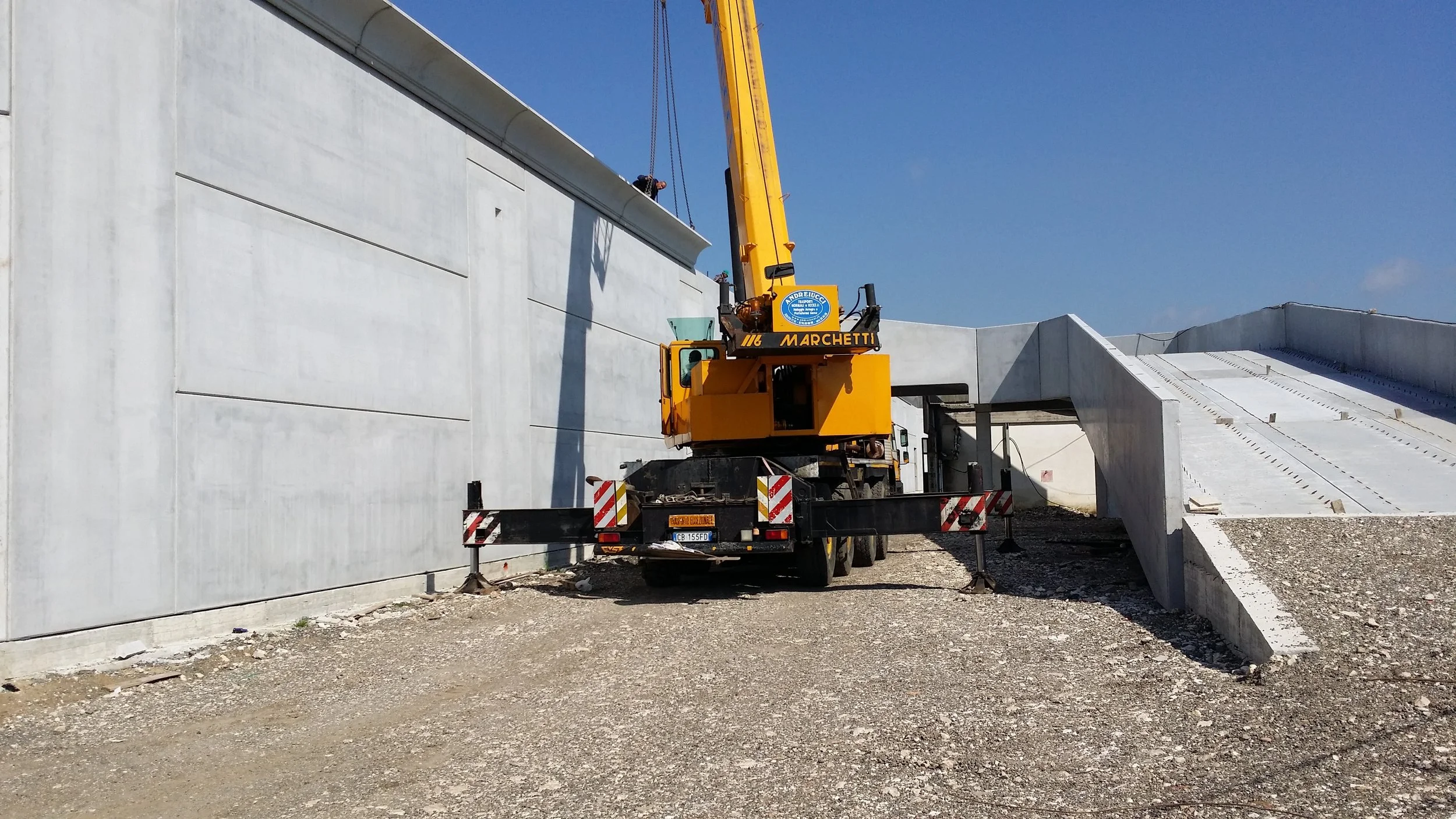 Cantiere con gru gialla che solleva materiali vicino a una struttura in cemento