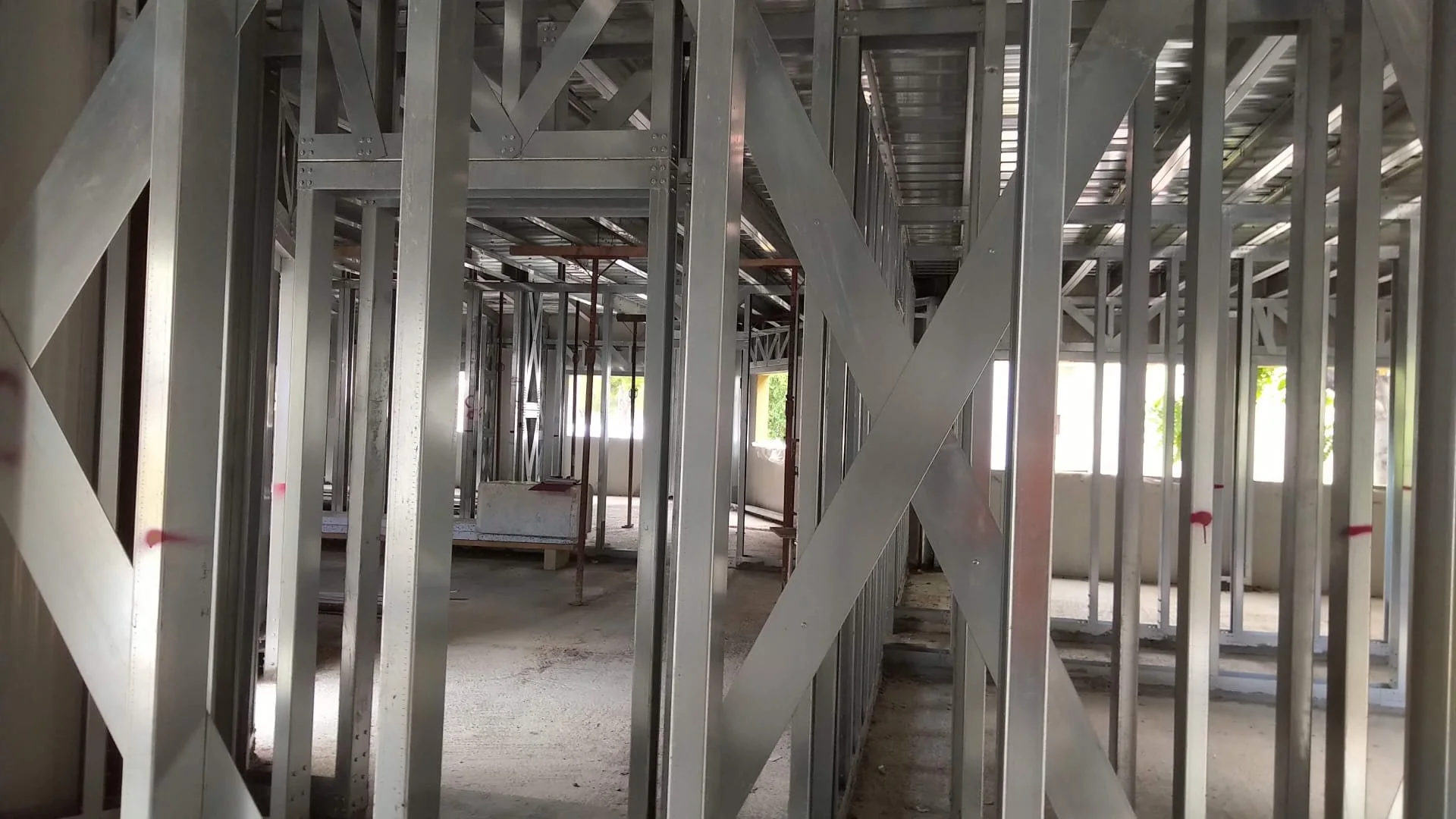 Struttura in acciaio in fase di costruzione in un edificio. Montanti, tracce e supporti metallici sono visibili, con finestre che lasciano entrare luce naturale.