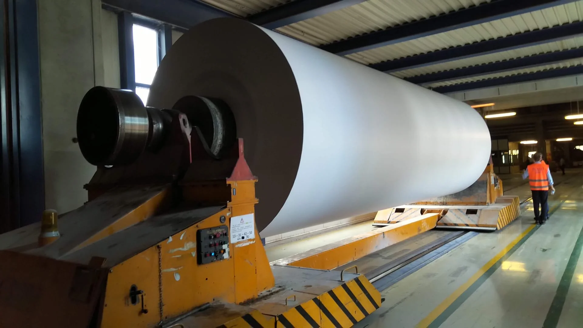 Grandi bobine di carta o altro materiale trasportata su un carro industriale in un ambiente di fabbrica o magazzino.