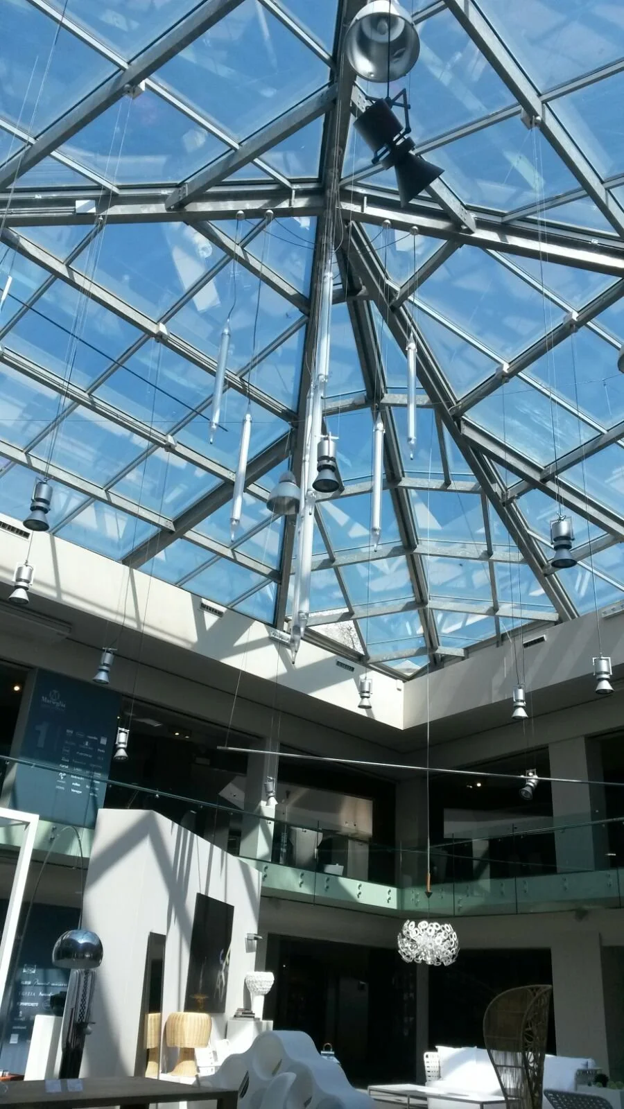 Il soffitto di una hall moderna con tetto in vetro e luci sospese, decorazioni di oggetti d'arte e mobili.