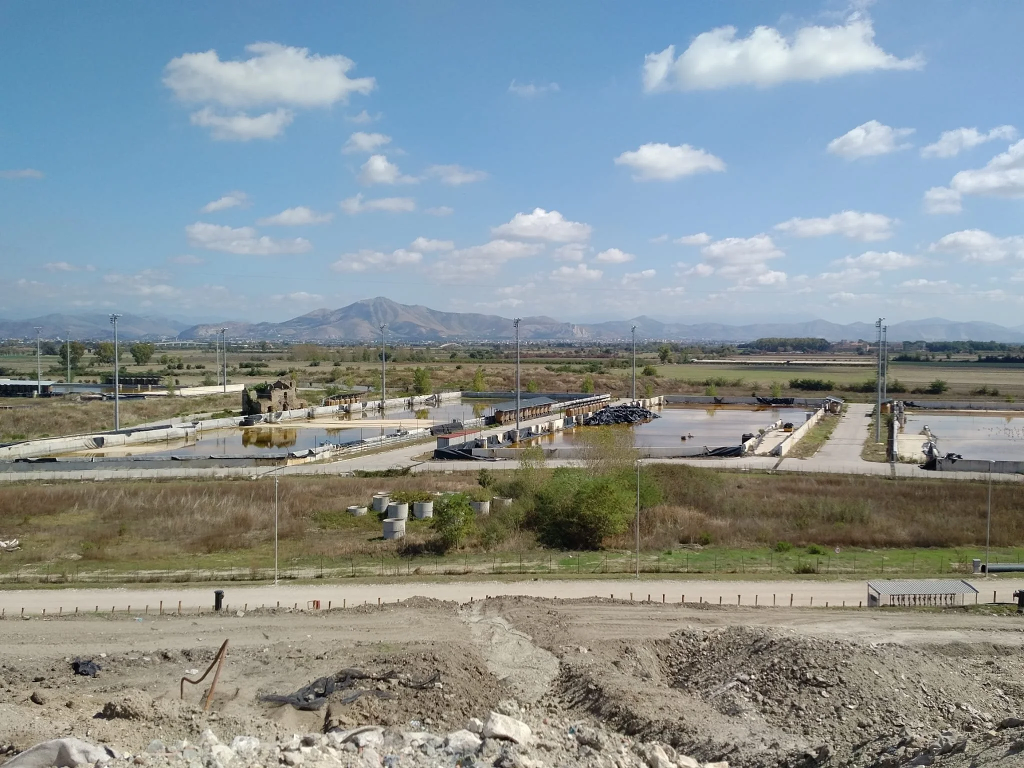 Paesaggio rurale con stagioni di raccolta, con un campo di saline e un paesaggio montuoso sullo sfondo, cielo sereno con alcune nuvole.