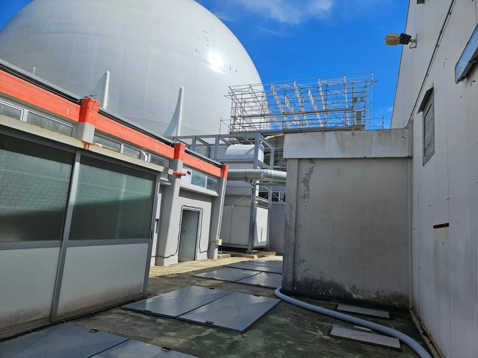 Immagine di un'area di tech infrastructure con strutture metalliche e edifici industriali, parte di un sito di telecomunicazioni o energia, sotto un cielo blu.