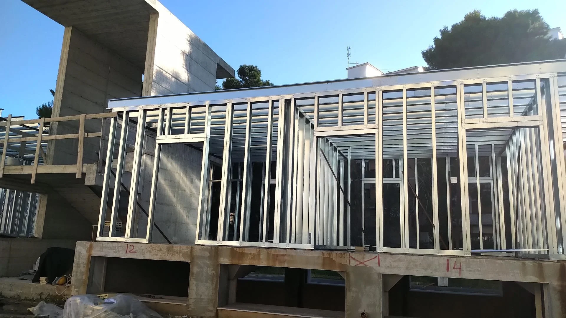 Struttura in costruzione di una casa con telai in metallo e cemento, con impalcature e finestre installate.