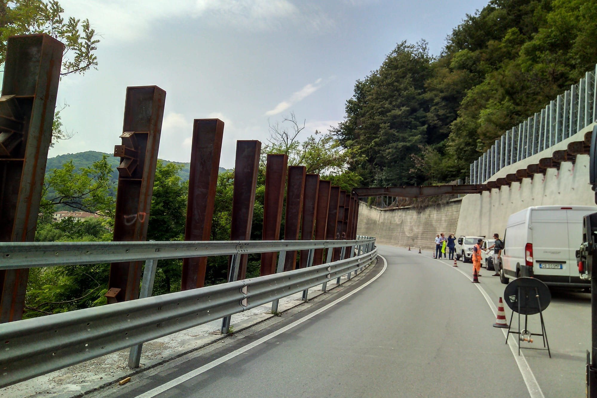 Costruzione sulla strada con barriere di sicurezza e veicoli in sosta, operai e segnali di lavoro che indicano lavori in corso