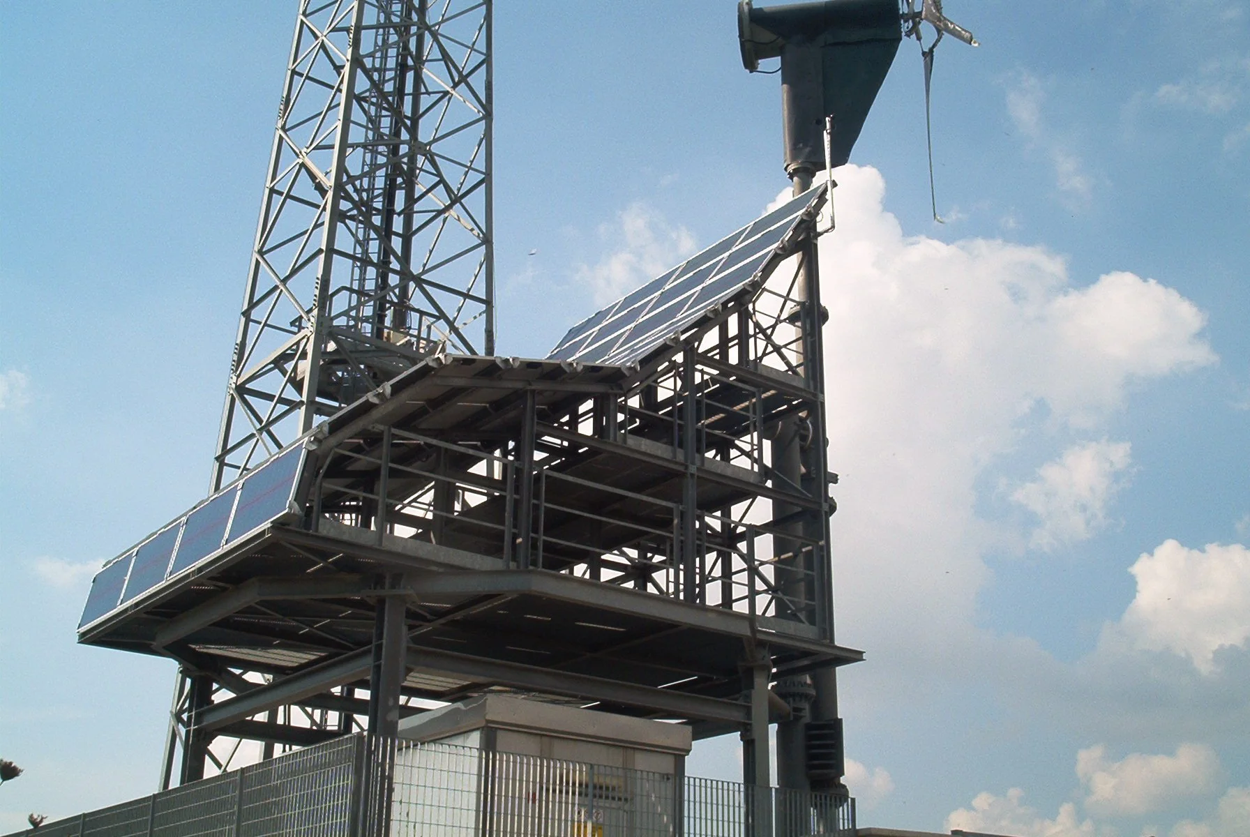 Gancio di una torre di telecomunicazioni con pannelli solari e struttura di metallo sotto un cielo con nuvole