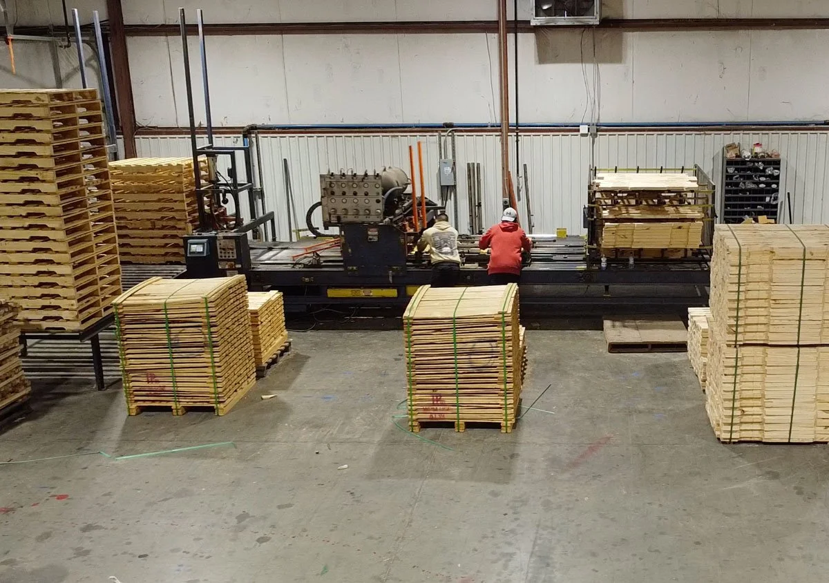 interior of woodcraft with 2 men working on a pallet assembly machine