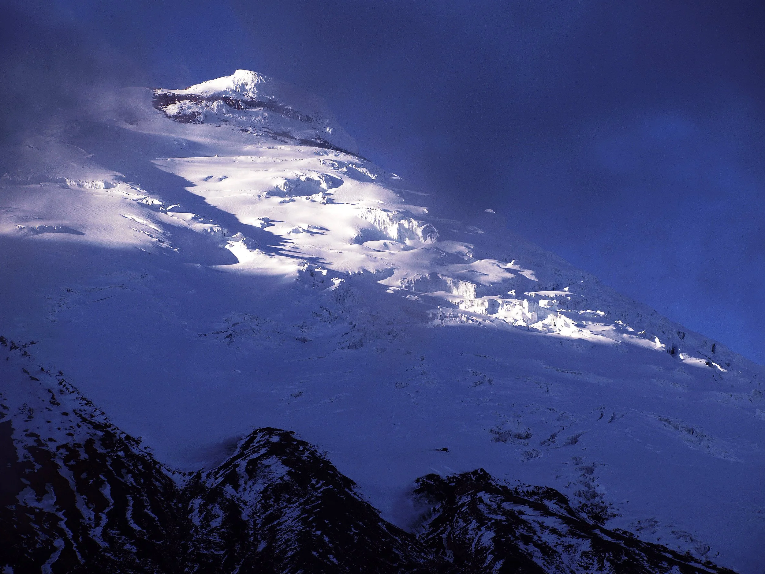 Snow-covered mountain peak with blue sky and clouds in the background.