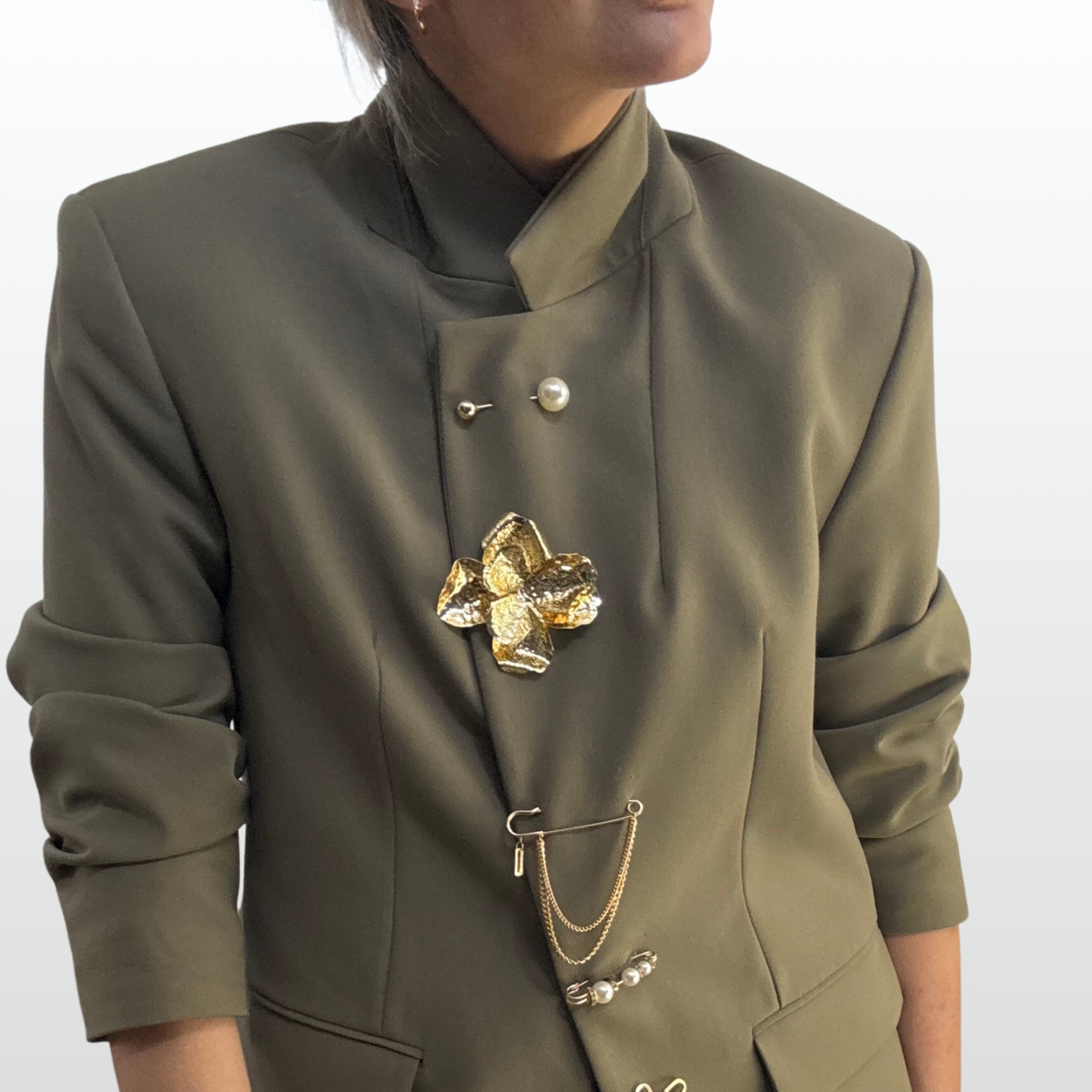 A gold brooch stack down the front of a model's blazer. Featuring pearl pins and an oversized flower brooch.