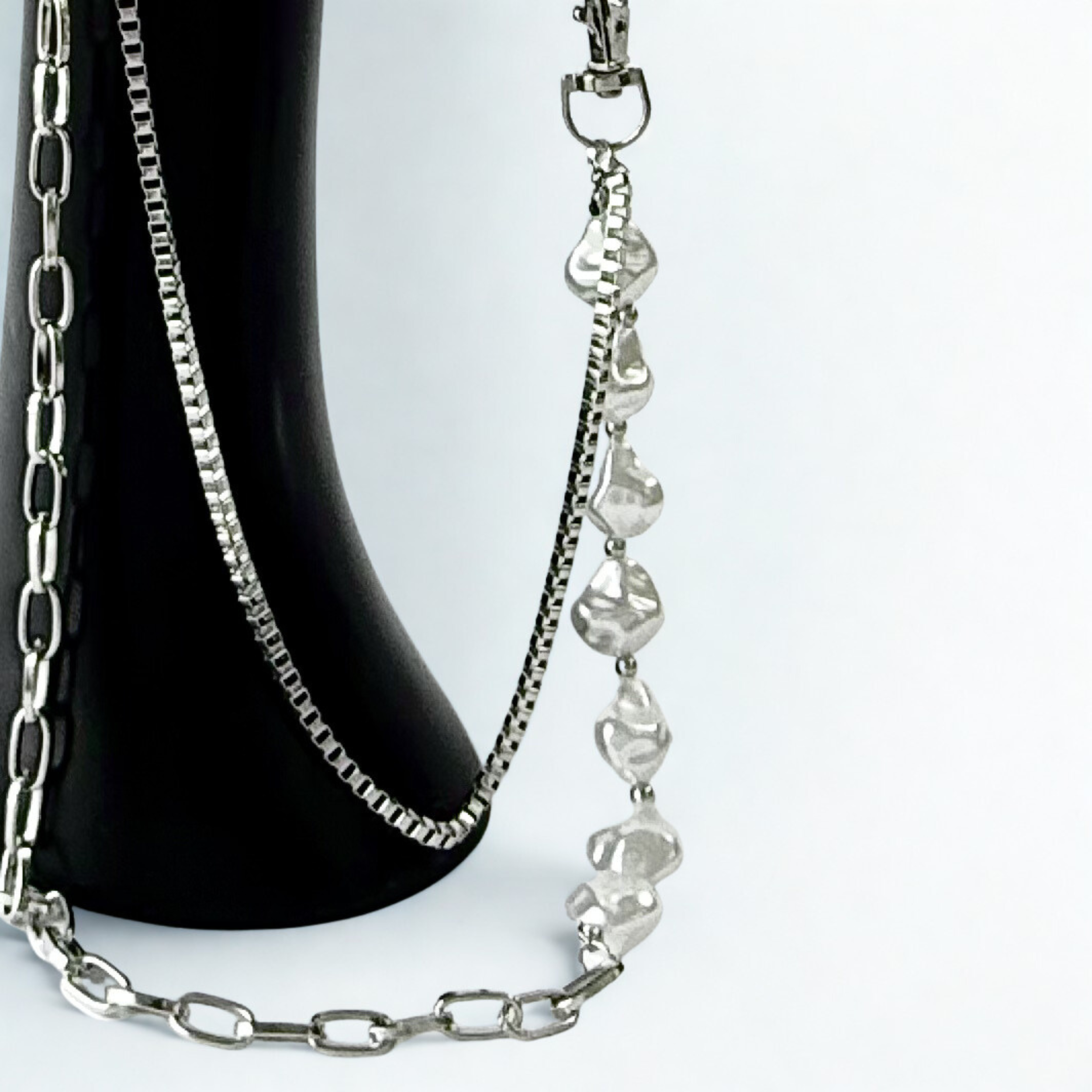 Close up of trouser chain which consists of two layered chains: a substantial, classic curb link and a delicate faux pearl chain.