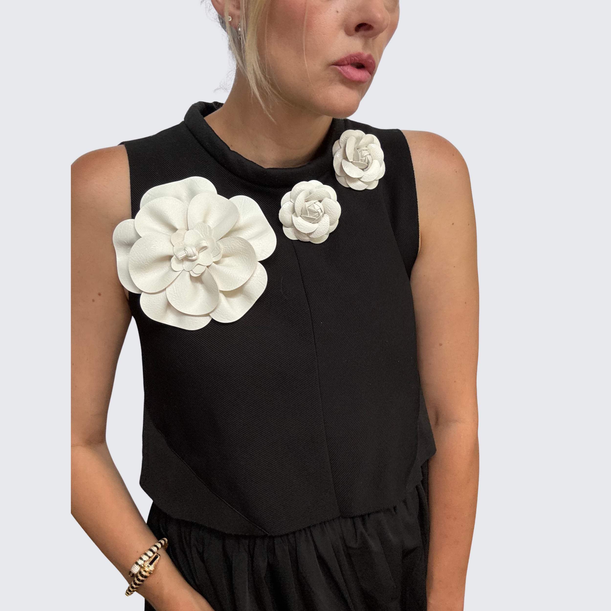 Close-up of woman wearing oversized white leather floral brooches on formal black sleeveless top.