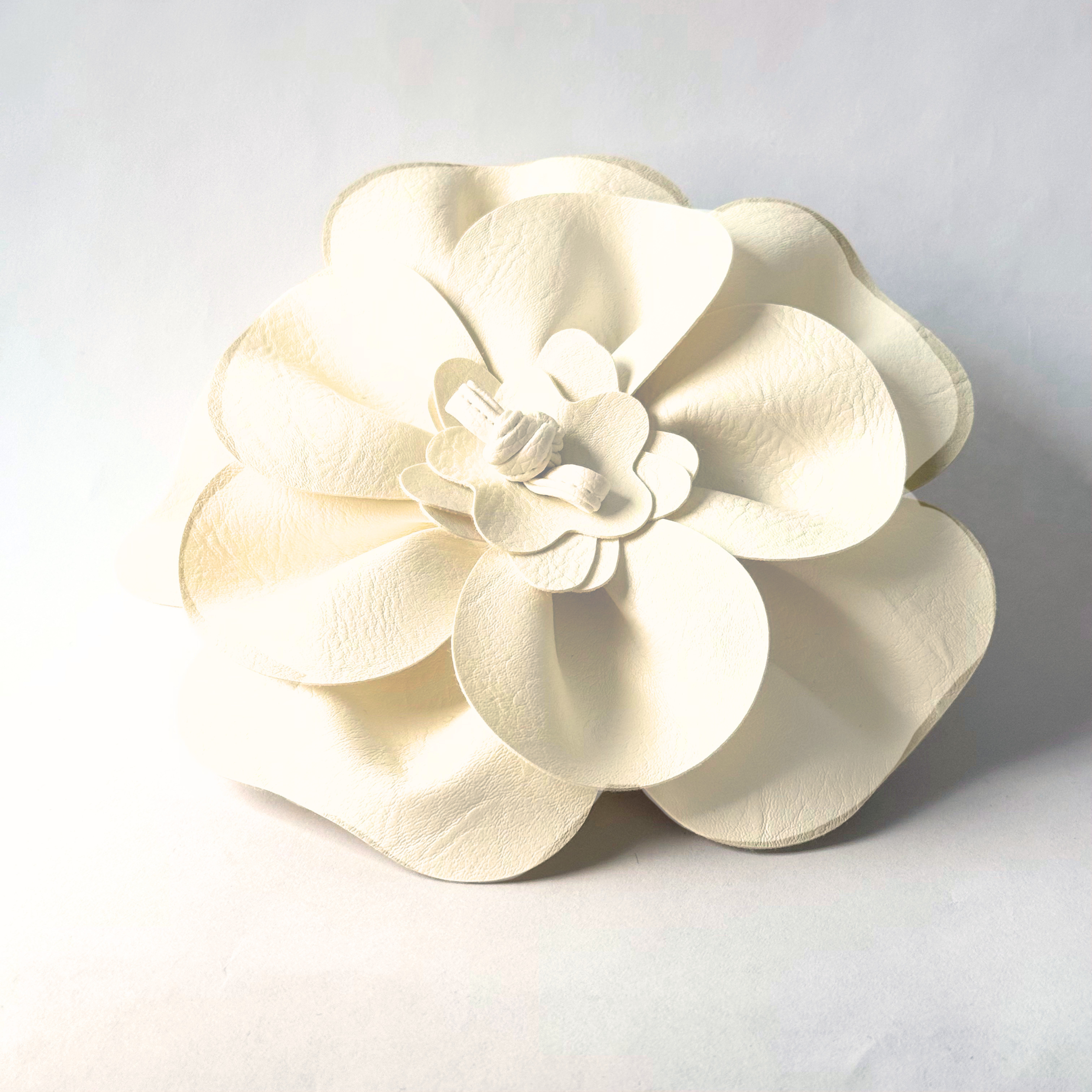 Close-up of woman wearing oversized cream leather floral brooch on white blazer.