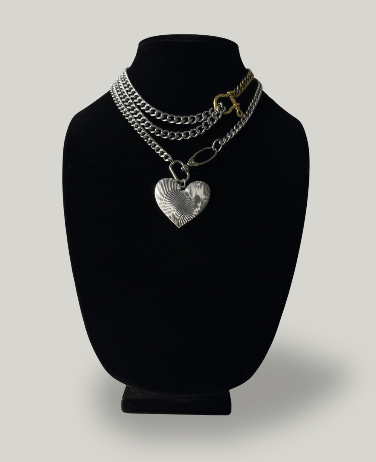 Silver layered chains with a heart-shaped pendant on a black jewelry display bust.