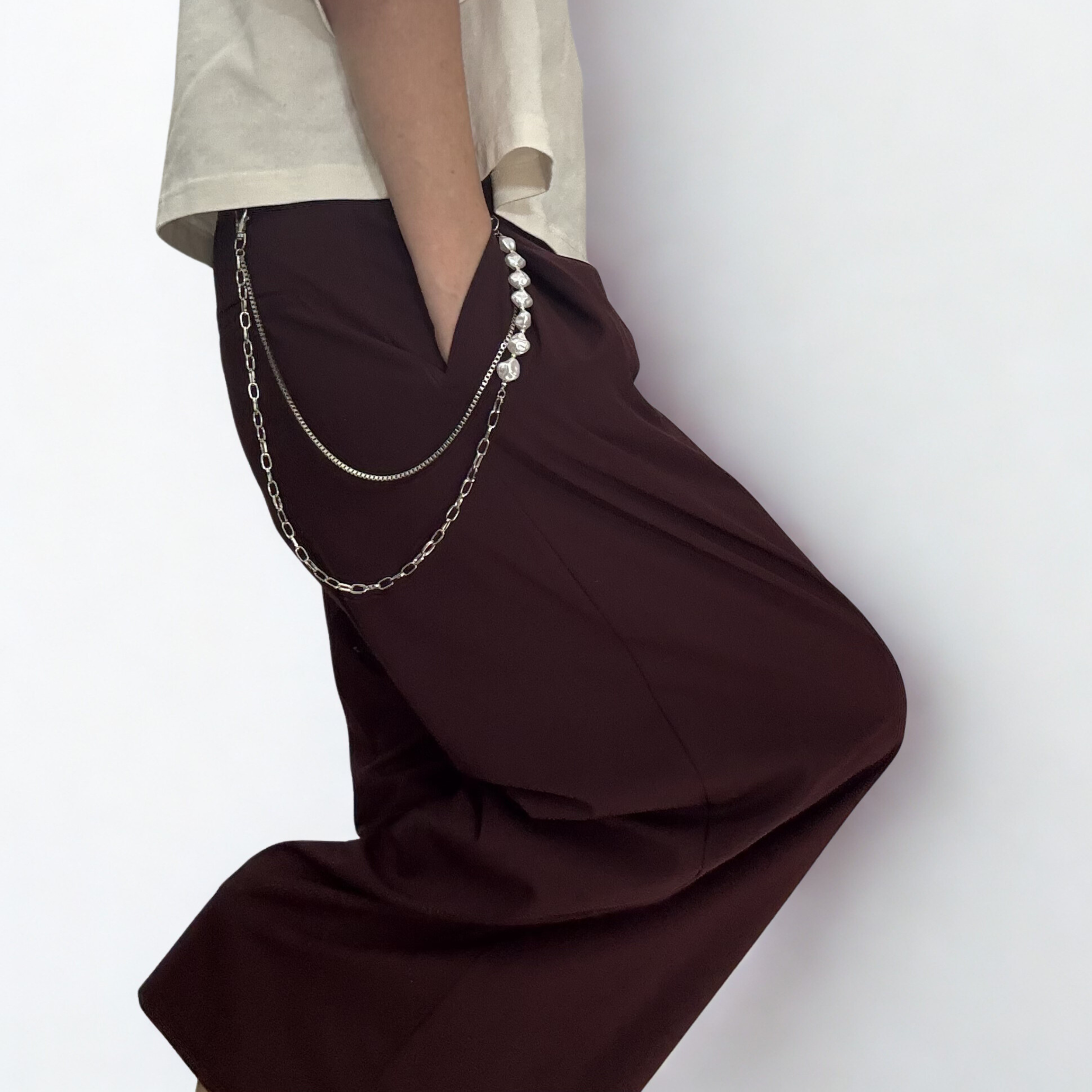 Trouser chain which consists of two layered chains: a substantial, classic curb link and a delicate faux pearl chain, styled on a pair of eggplant trousers.