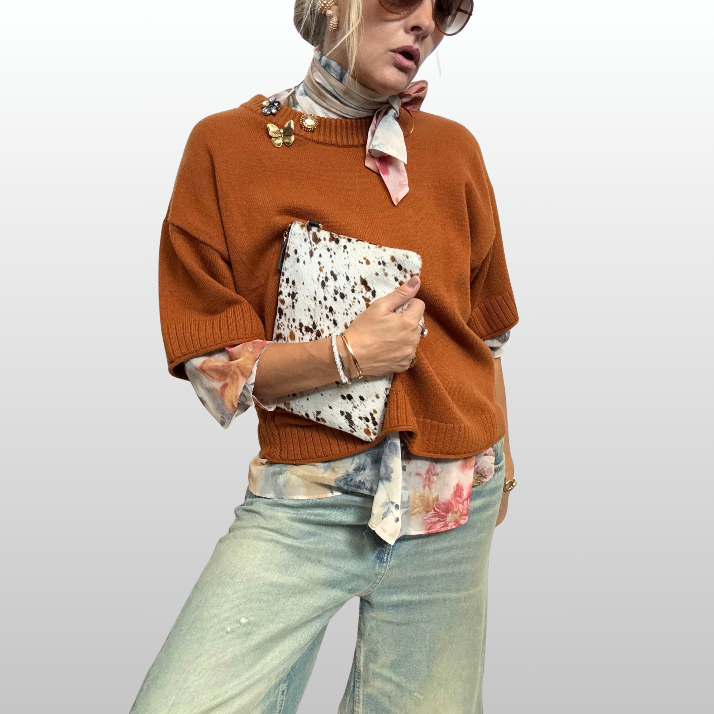 A close up of a woman wearing an amber knit over a sheer floral shirt with a necktie. The collar of the knit is accented by a cluster of three amber and golden brooches from The Brooch House.