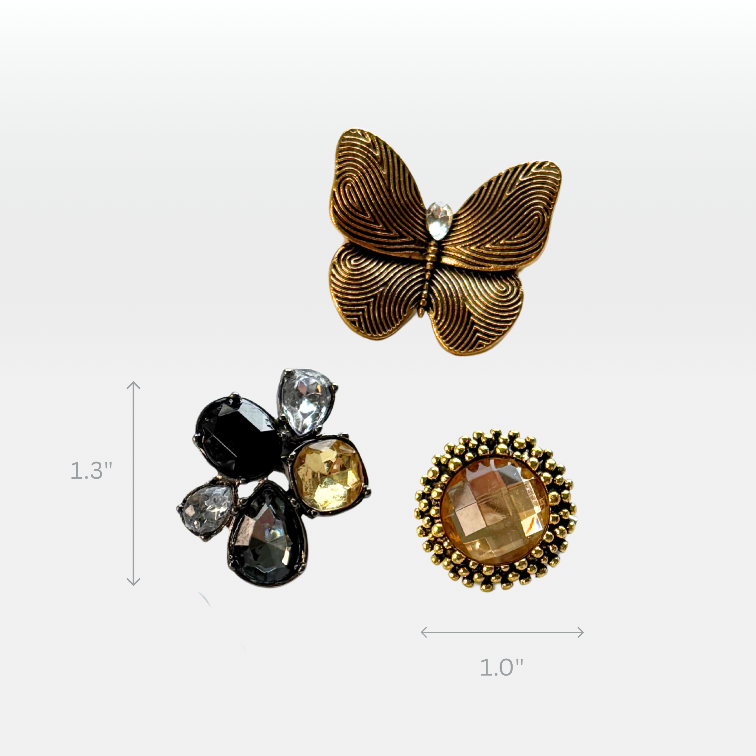 Close up of three brooches.  A small golden butterfly, an amber stud with golden border, and an amber and charcoal crystal teardrop cluster.