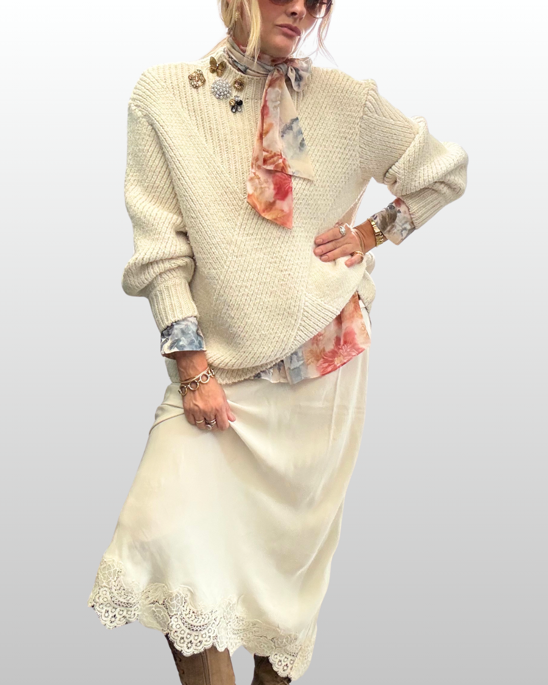 Playful boho-inspired shoulder brooch stack on a cream cable-knit sweater paired with a lace-trimmed skirt and boots.