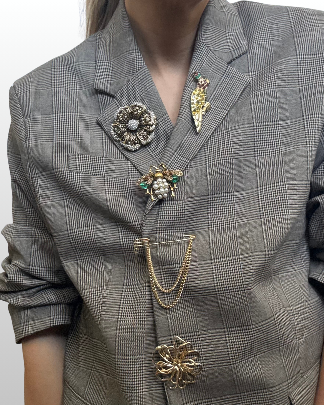 A layered brooch stack combining multiple heavy silver hardware pins and delicate pearl accents on a blazer lapel.