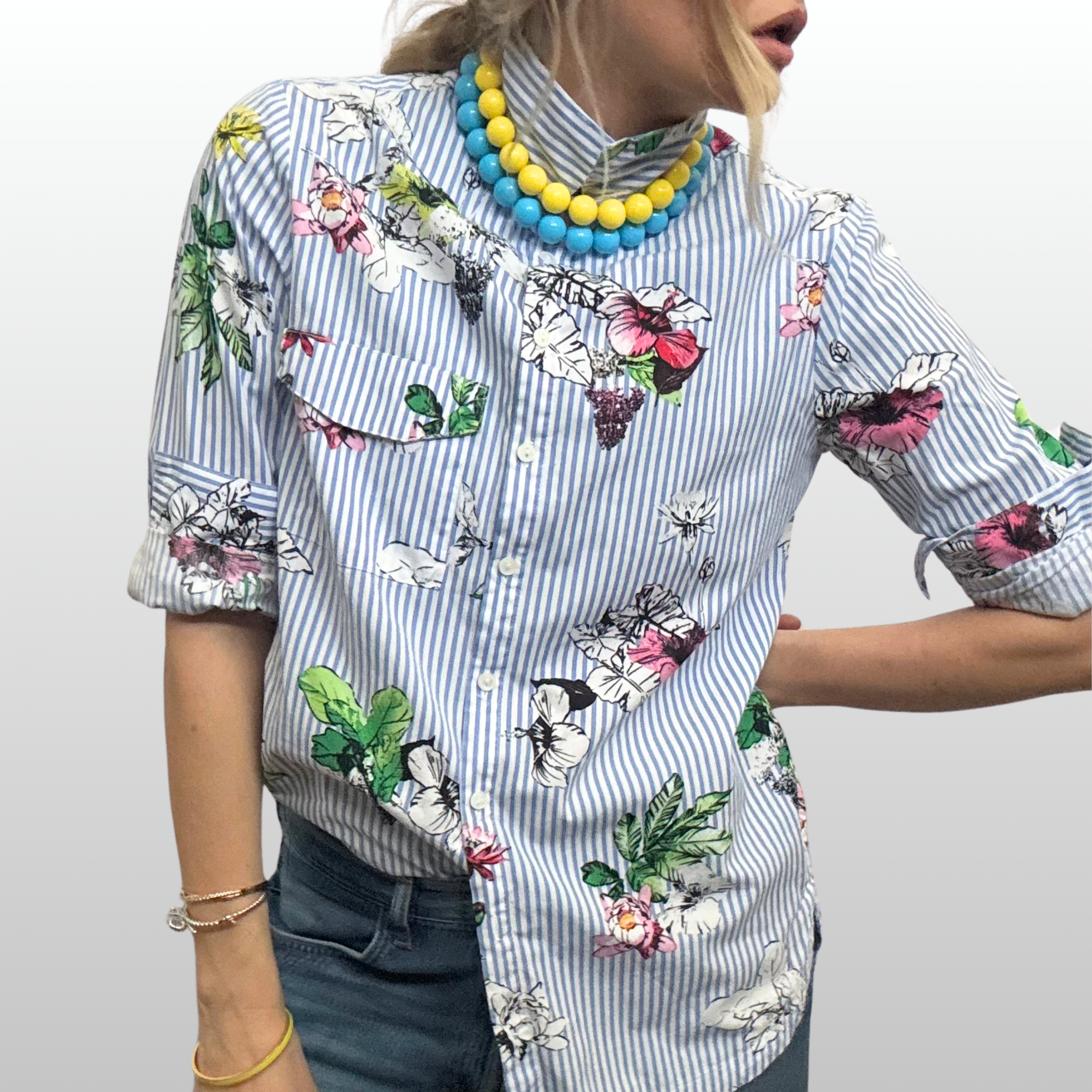 Woman wearing blue and white striped shirt with floral design on it. She is also wearing two strands of resin beaded necklaces - one blue and one yellow.