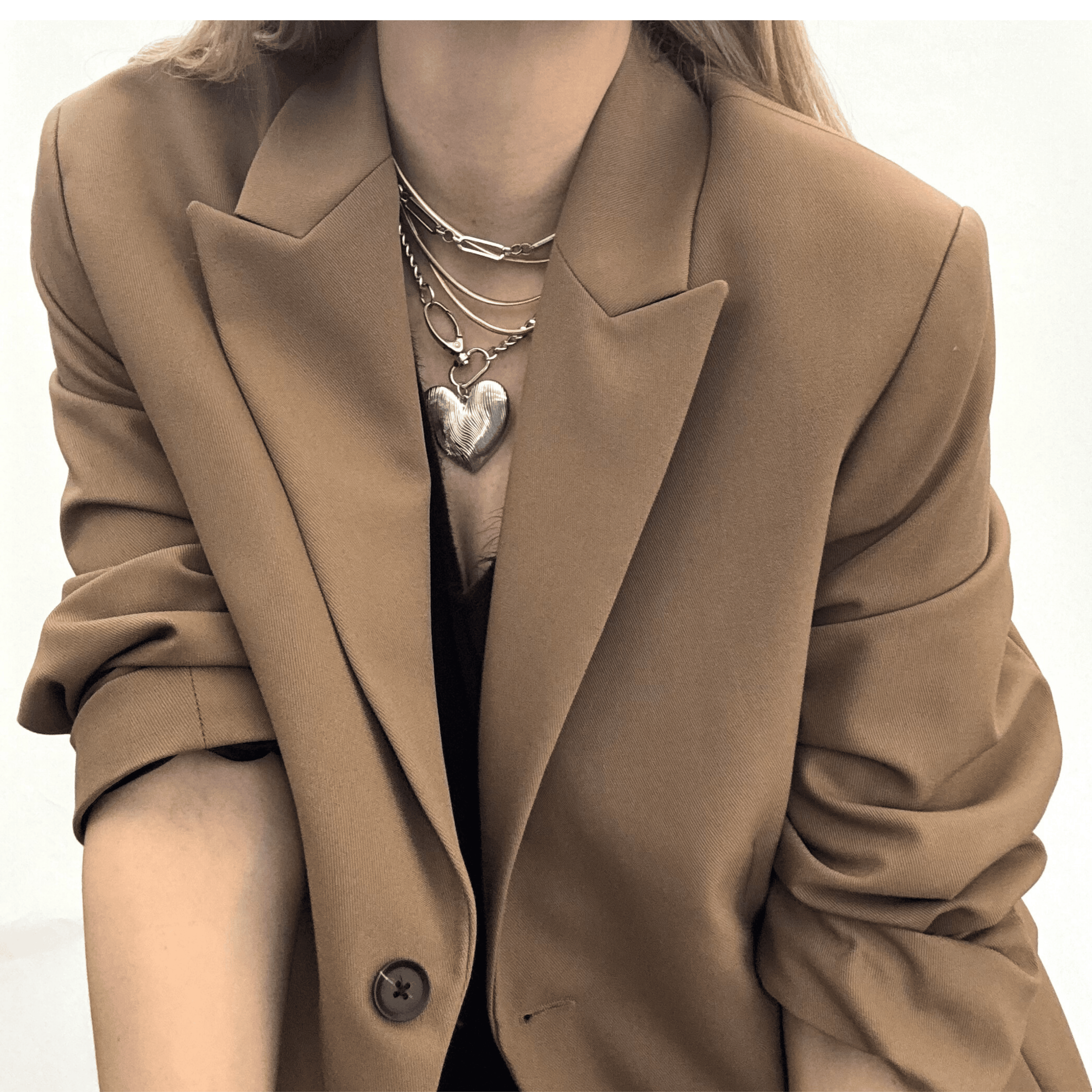 Silver etched oversized heart pendant layered with steel chains and styled with a neutral blazer.
