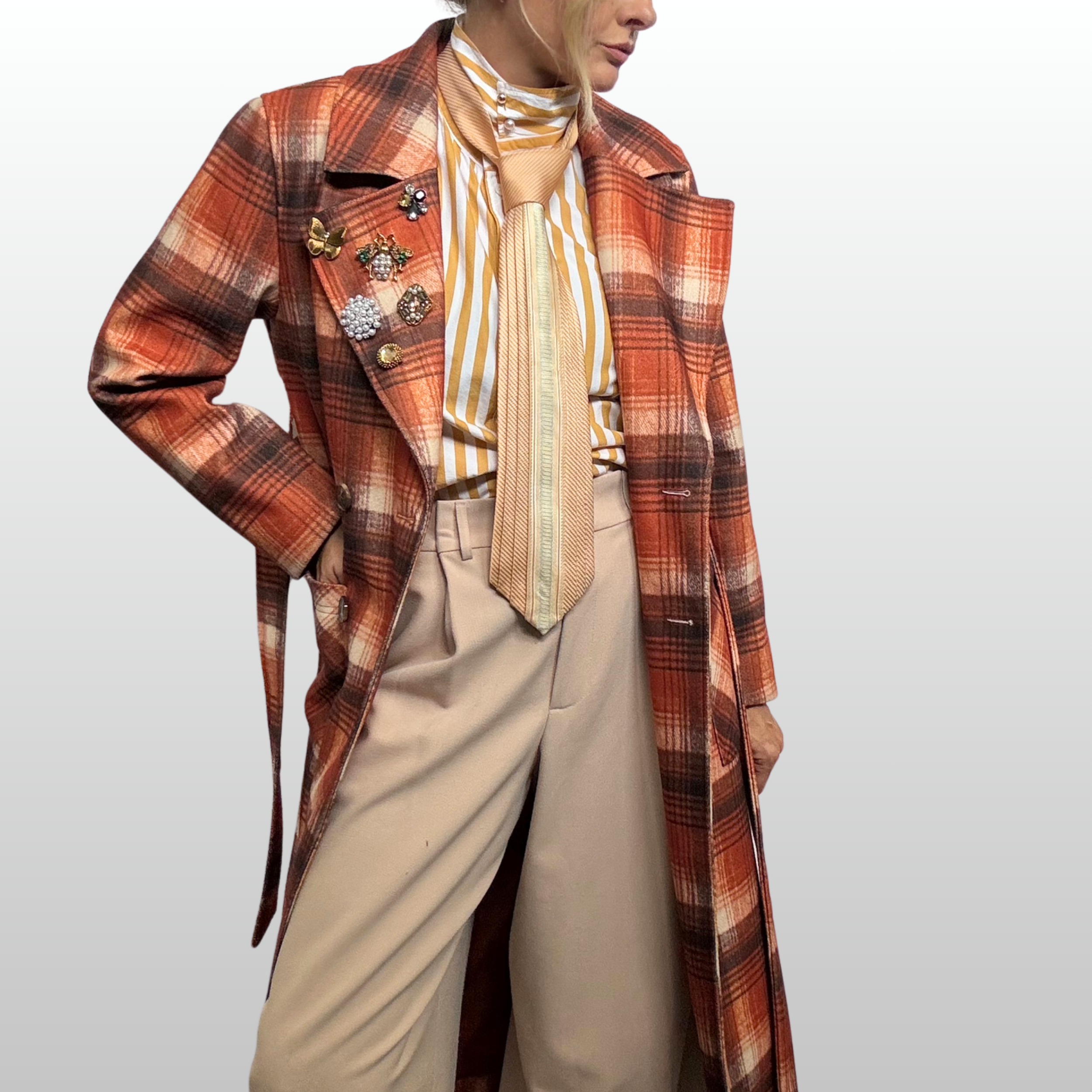 Woman wearing orange and amber hued plaid trench with 6 small amber and golden brooches clustered on her right lapel.