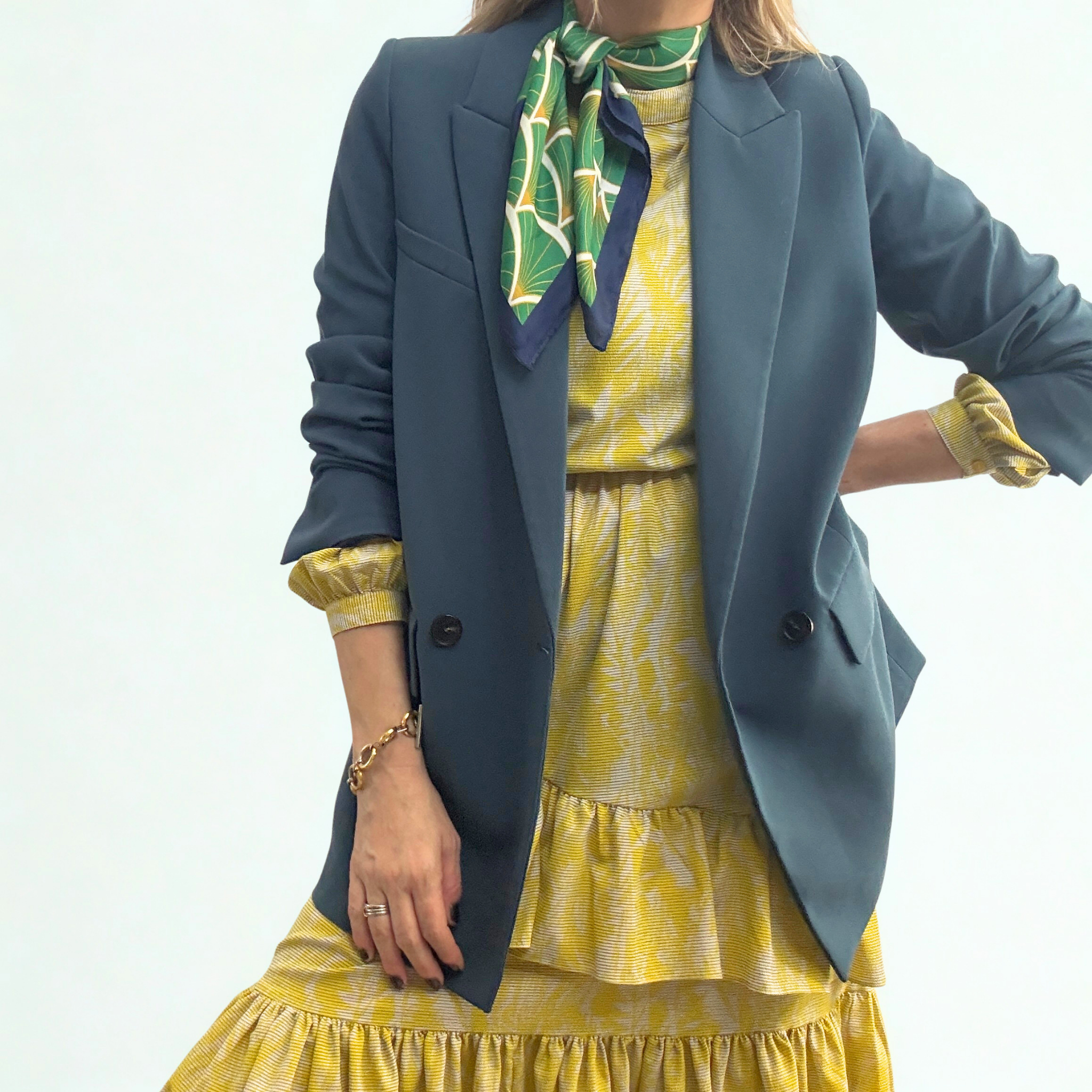 A rich, deep emerald green scarf with a soft, matte lustre styled in a loose knot around the neck to contrast a yellow patterned dress..