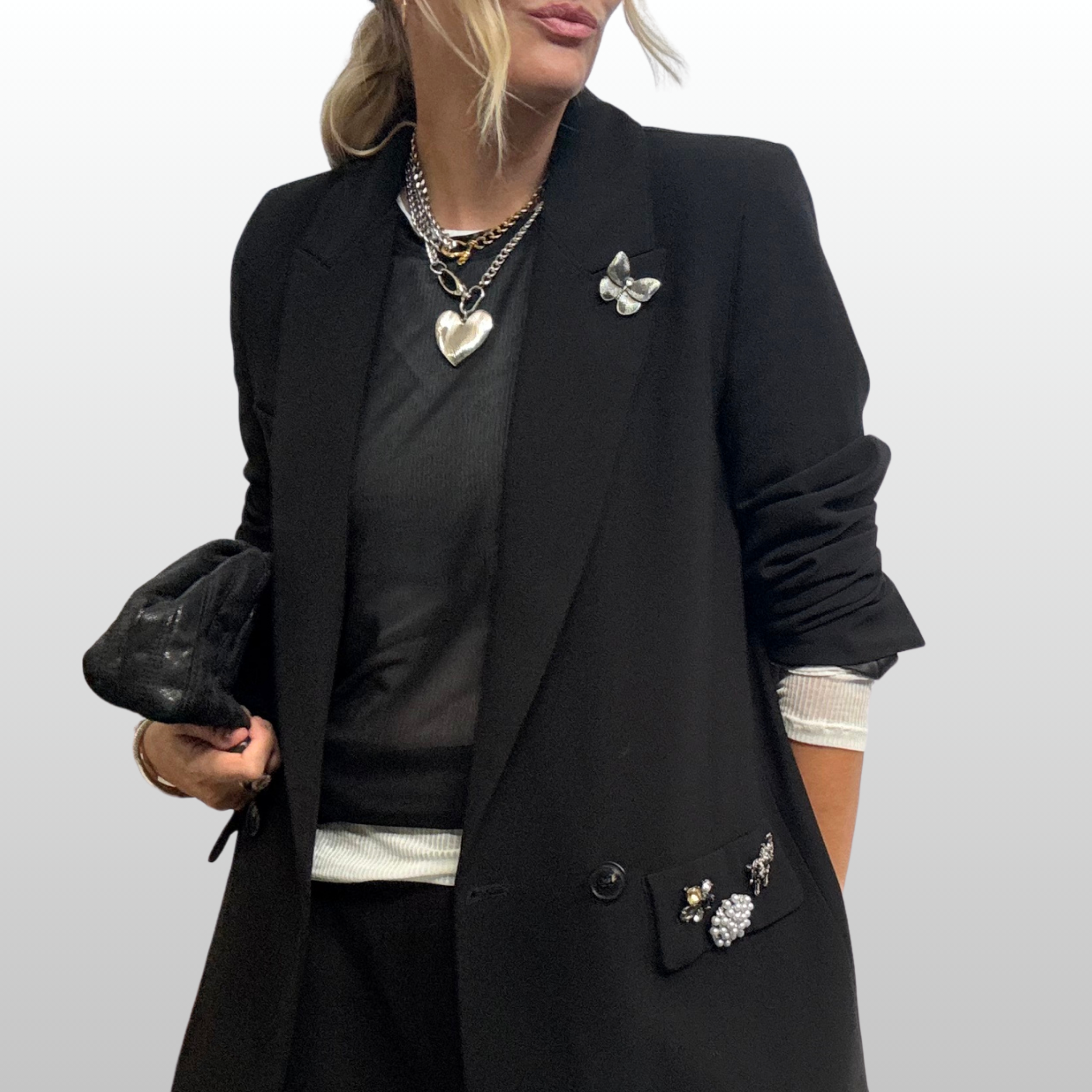 Woman wearing black blazer with silver statement necklaces and a small silver butterfly brooch on her lapel.
