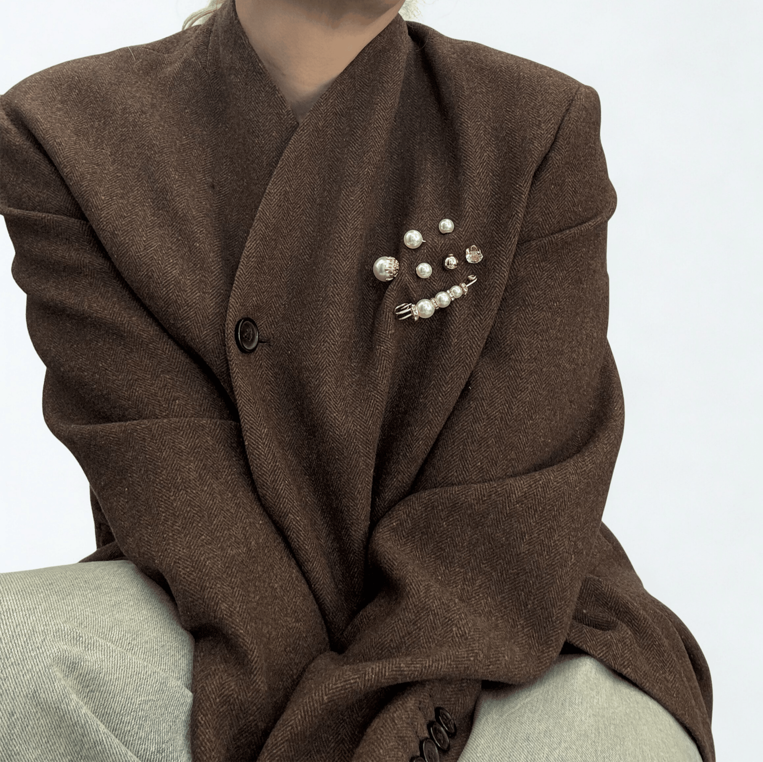 Person wearing a brown coat with pearl brooches.