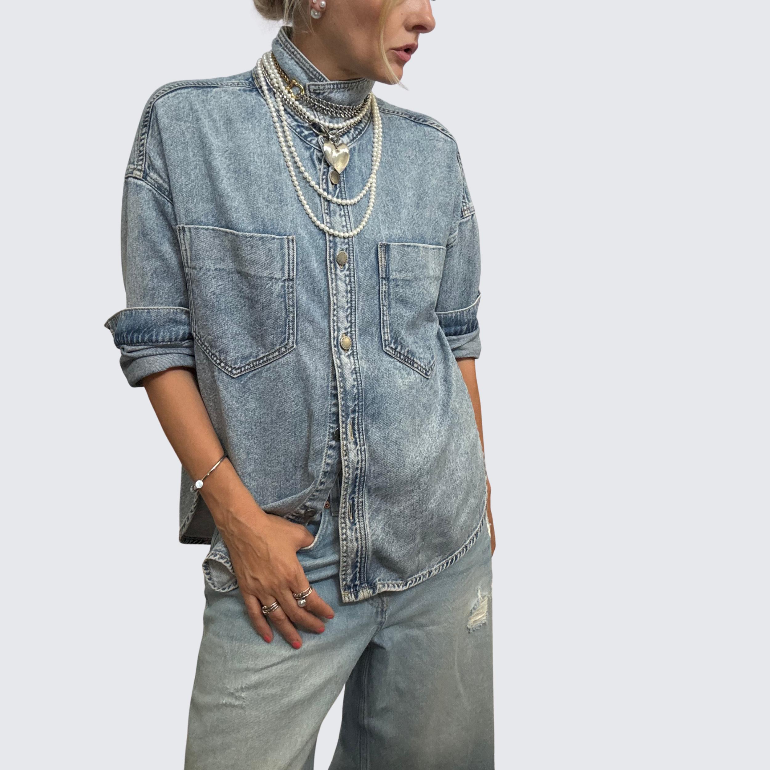 Woman wearing denim shirt with collar flipped up.  Over the collar she is wearing a mixed media necklace stack including pearls and chunky silver and gold statement necklaces from The Brooch House.