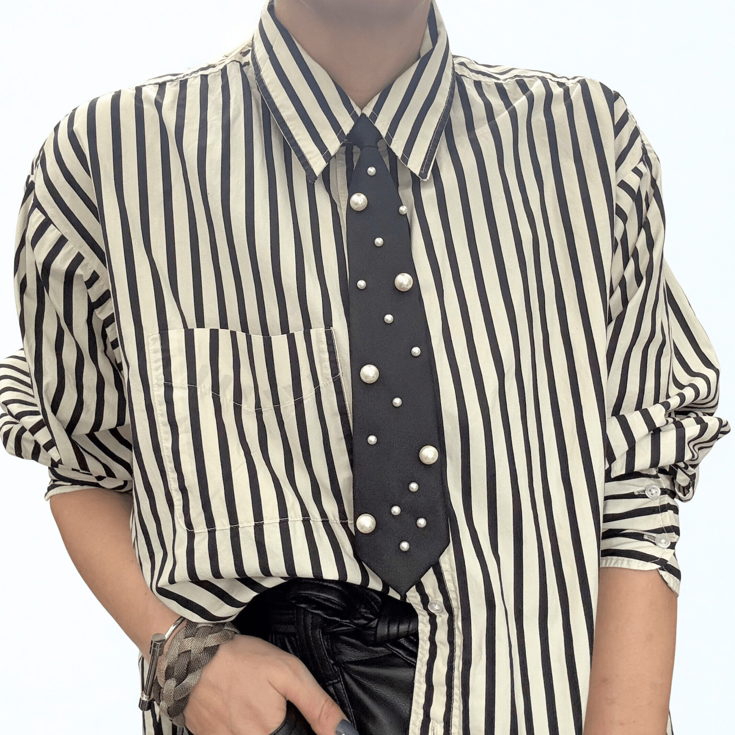 Person wearing a vertically striped black and white shirt with a black tie decorated with pearl-like beads, and black leather gloves.