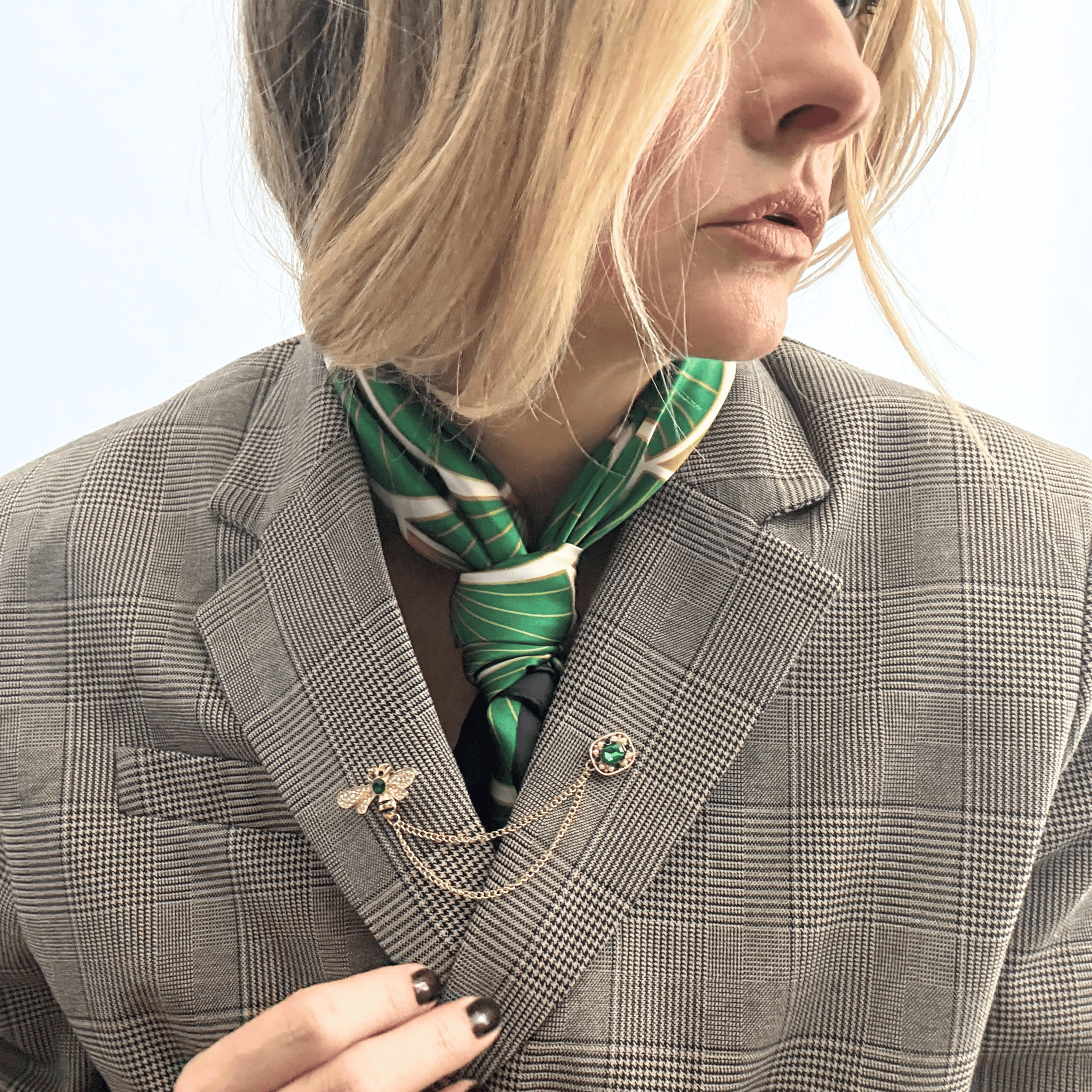 A rich, deep emerald green square scarf with a soft, matte lustre styled in a loose knot around the neck with an oversized plaid blazer..
