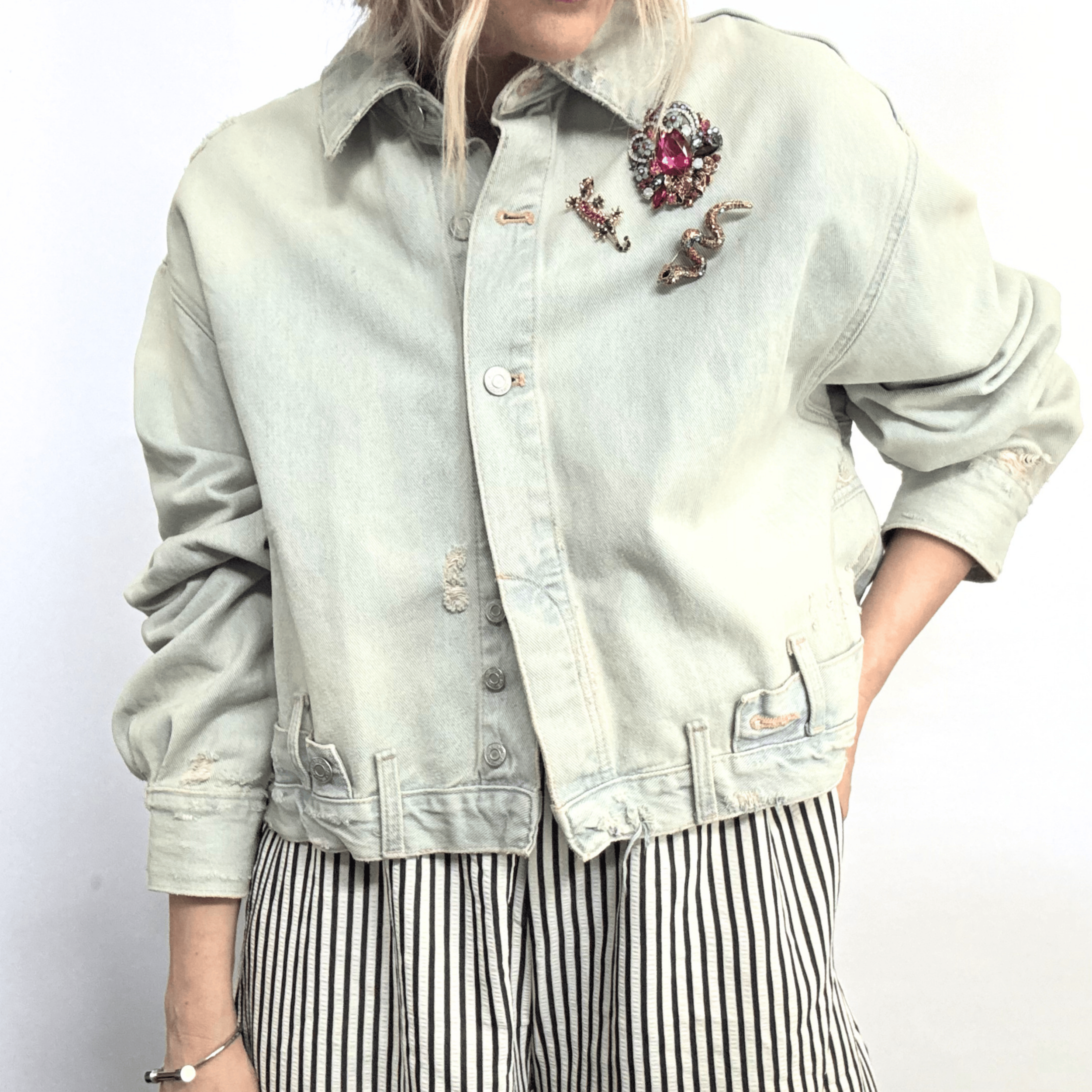 A cluster of jewel toned brooches on the lapel of a denim jacket. Cluster includes The Serpentine Prism Brooch and The Kaleidoscope Climber Brooch.