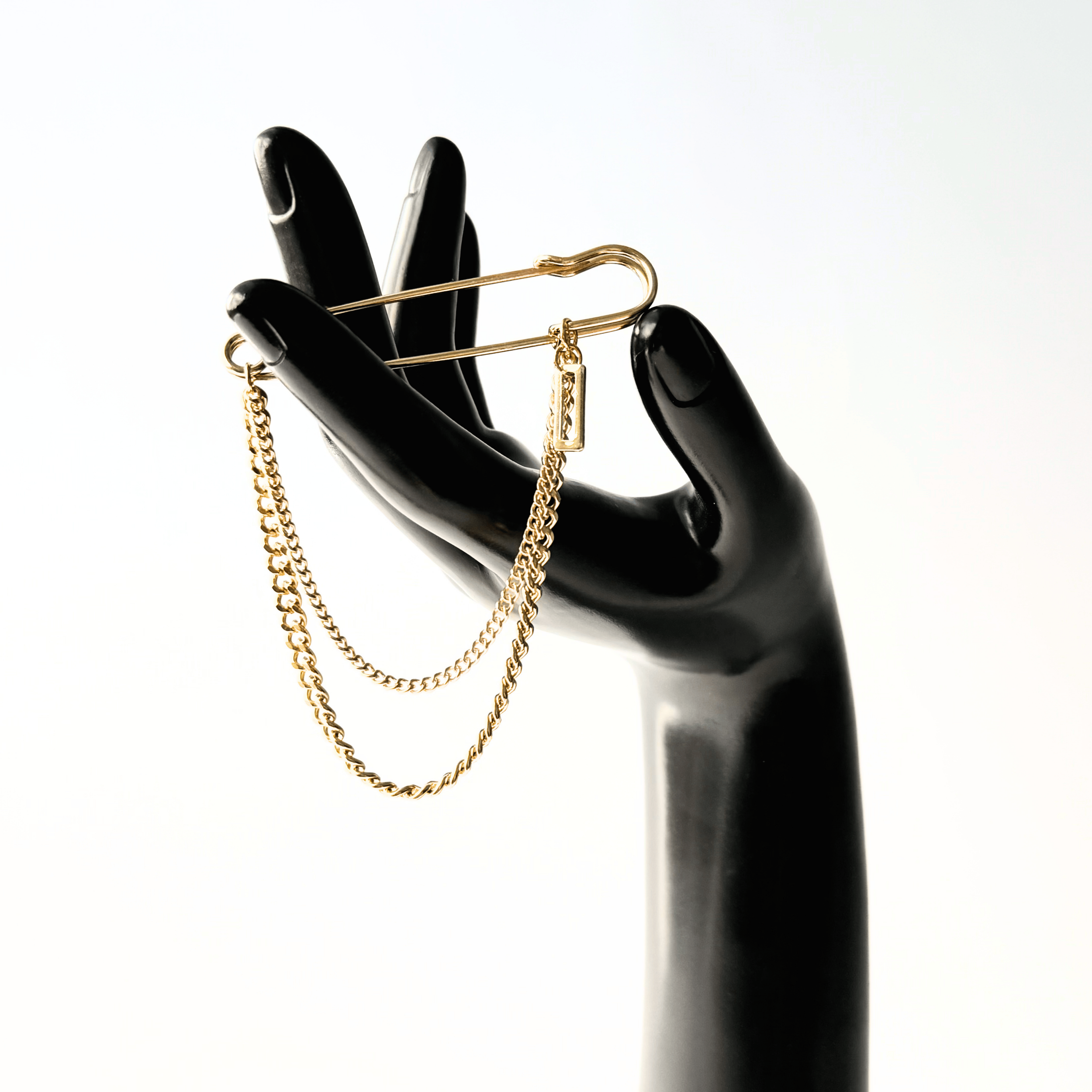 Close up of hand model holding a gold safety pin chain brooch.