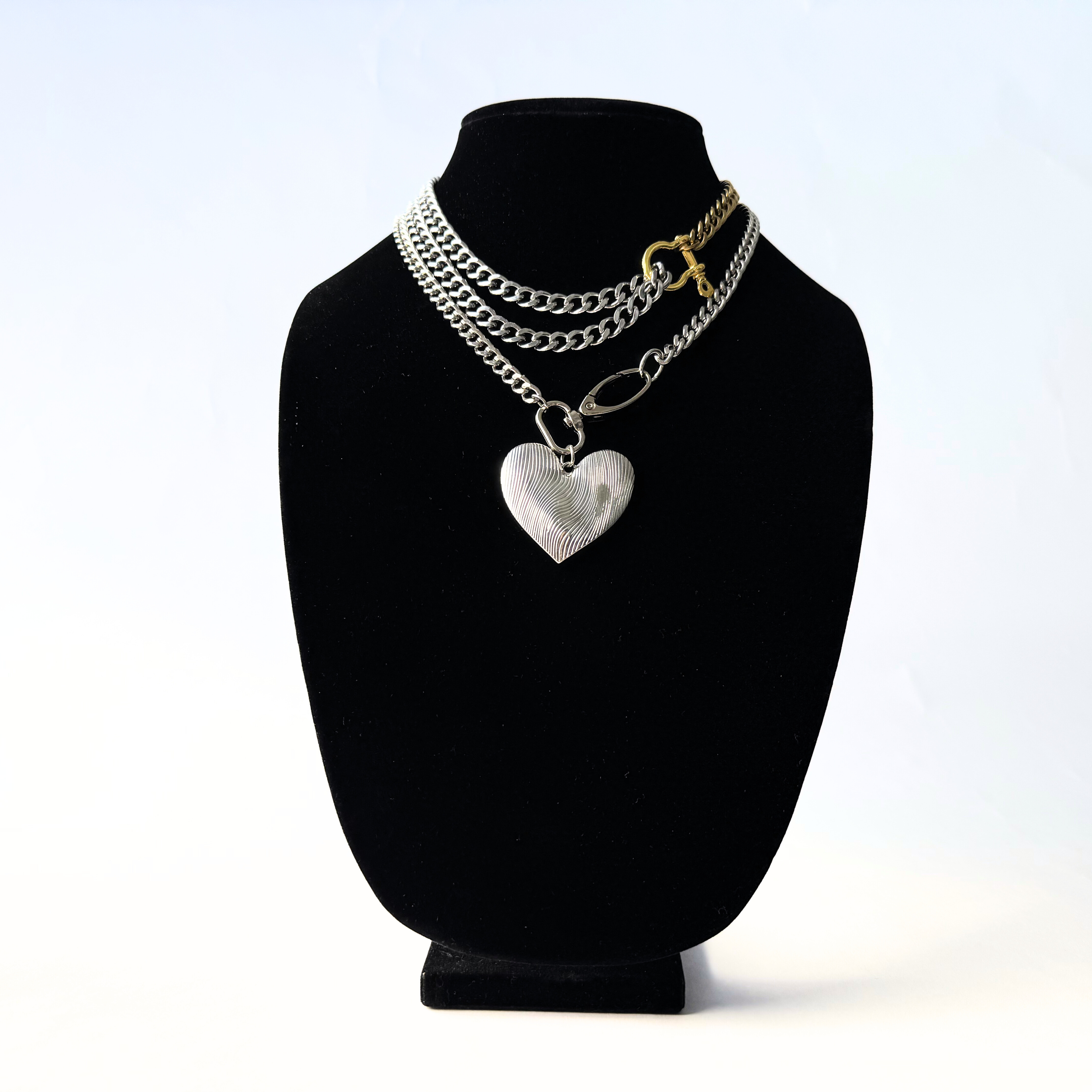 A bold, carabiner-style junction on a substantial, high-shine curb link chain, layered with an oversized etched silver heart pendant.