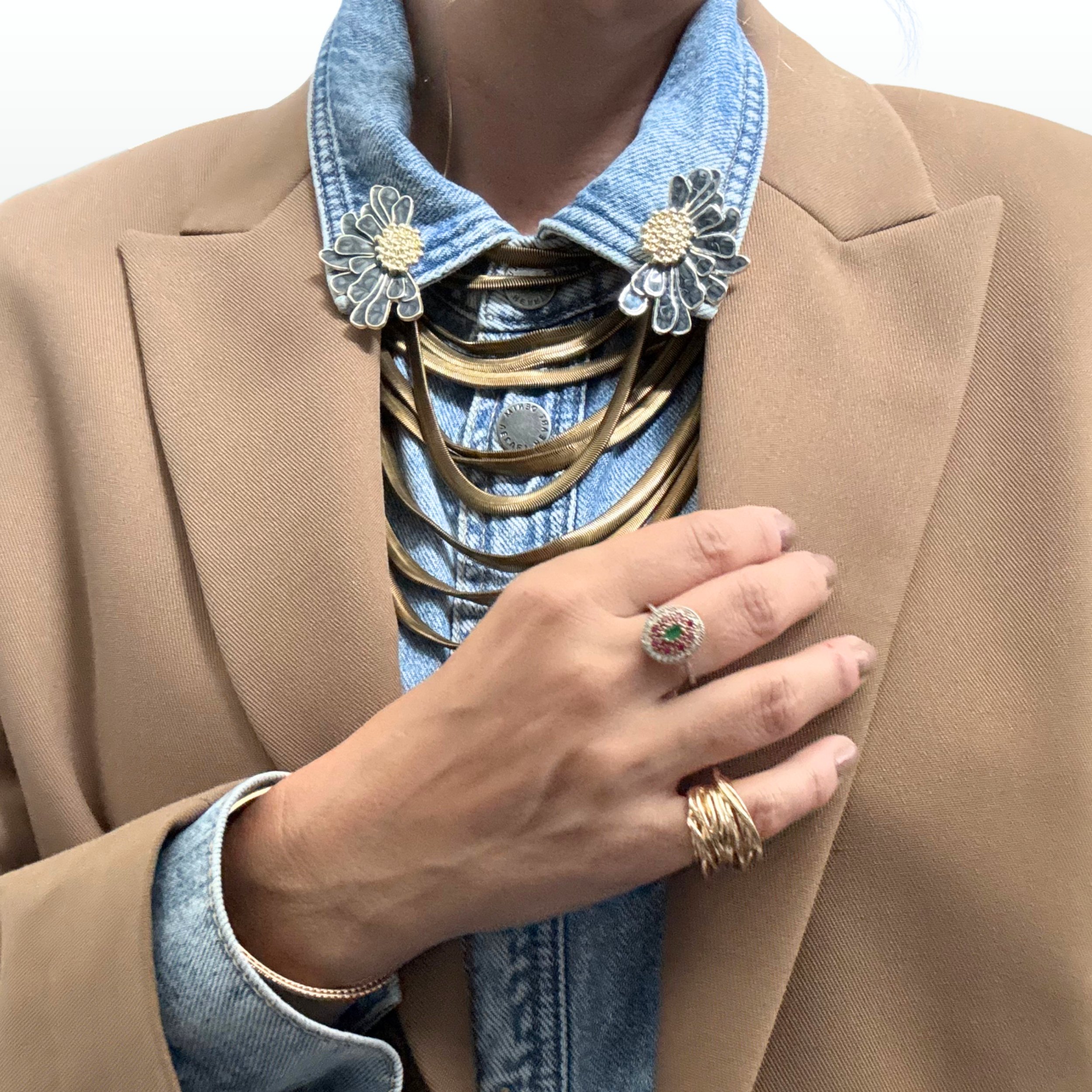 Close up of woman wearing statement ring with an emerald centre surrounded by ruby pink gemstones and golden pave.