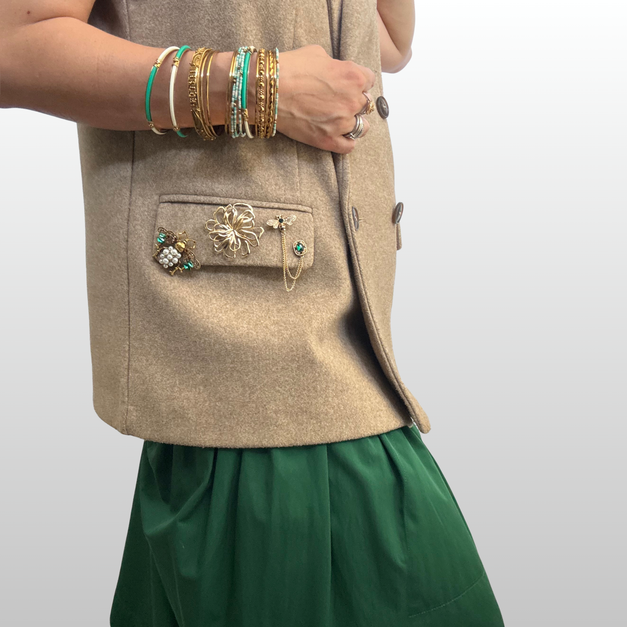 A close up of woman wearing a brown sleeveless blazer with three brooches layered on picket flap.