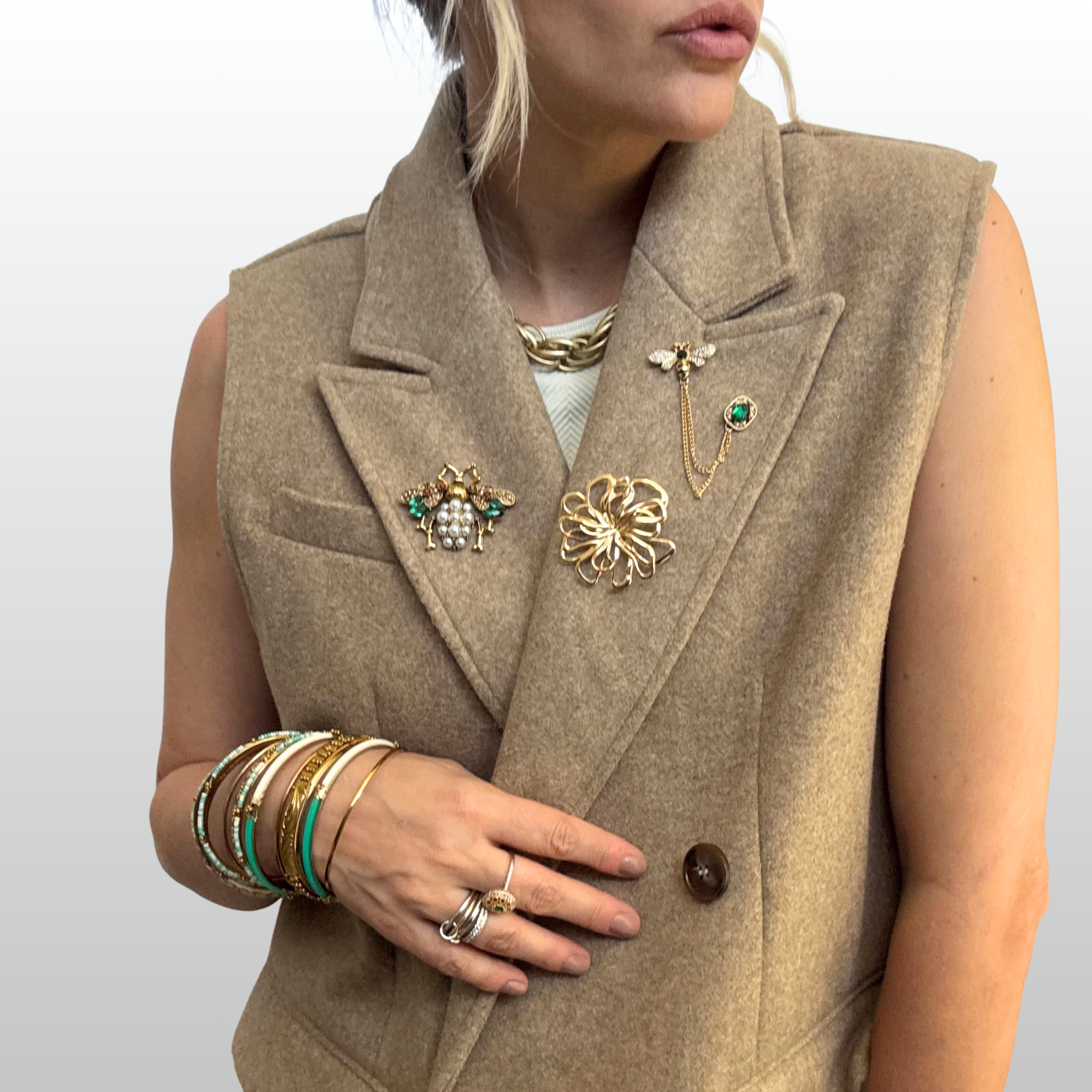 A close up of woman wearing a brown sleeveless blazer with three brooches layered on lapel.