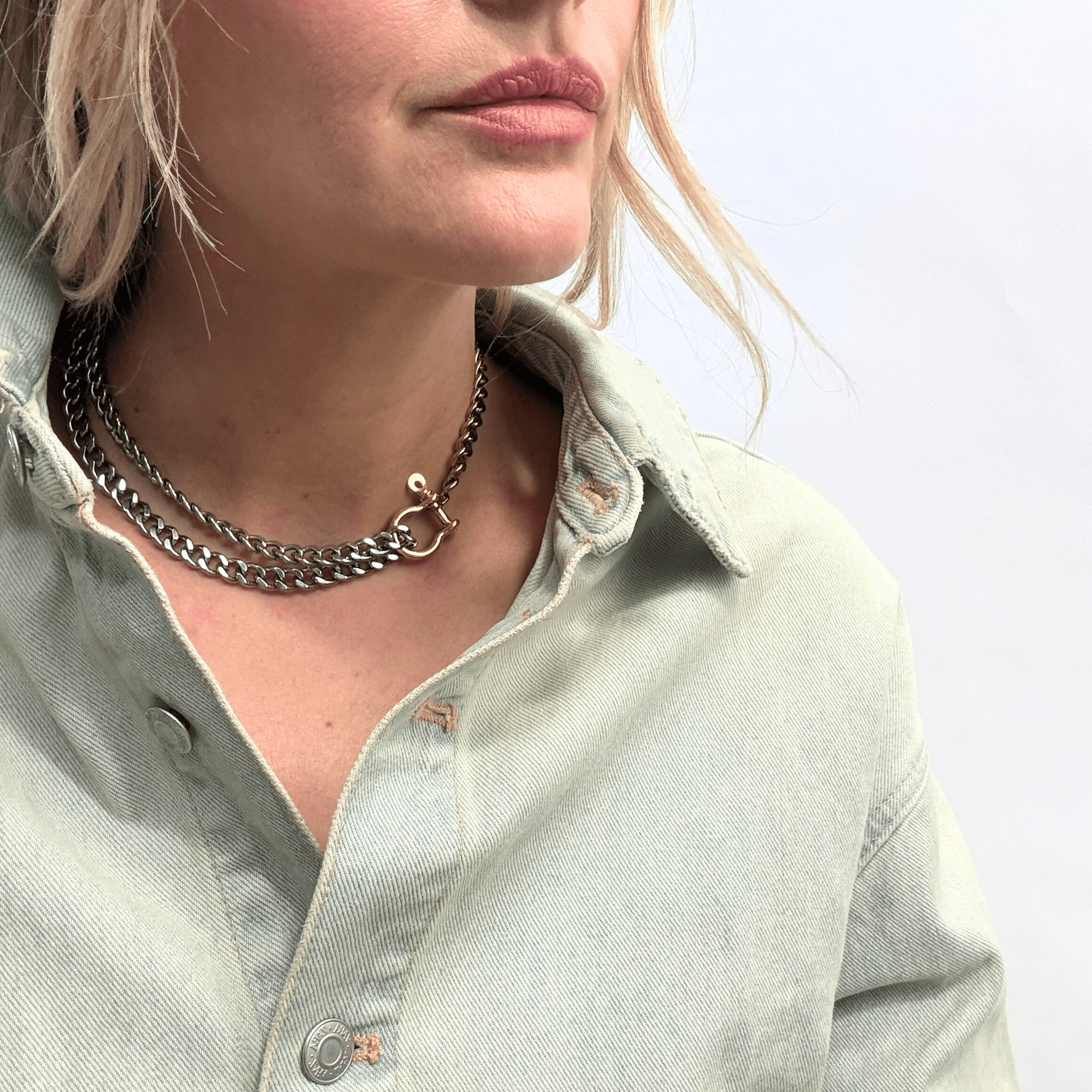 A bold, carabiner-style junction on a substantial, high-shine curb link chain, styled with a denim jecket.