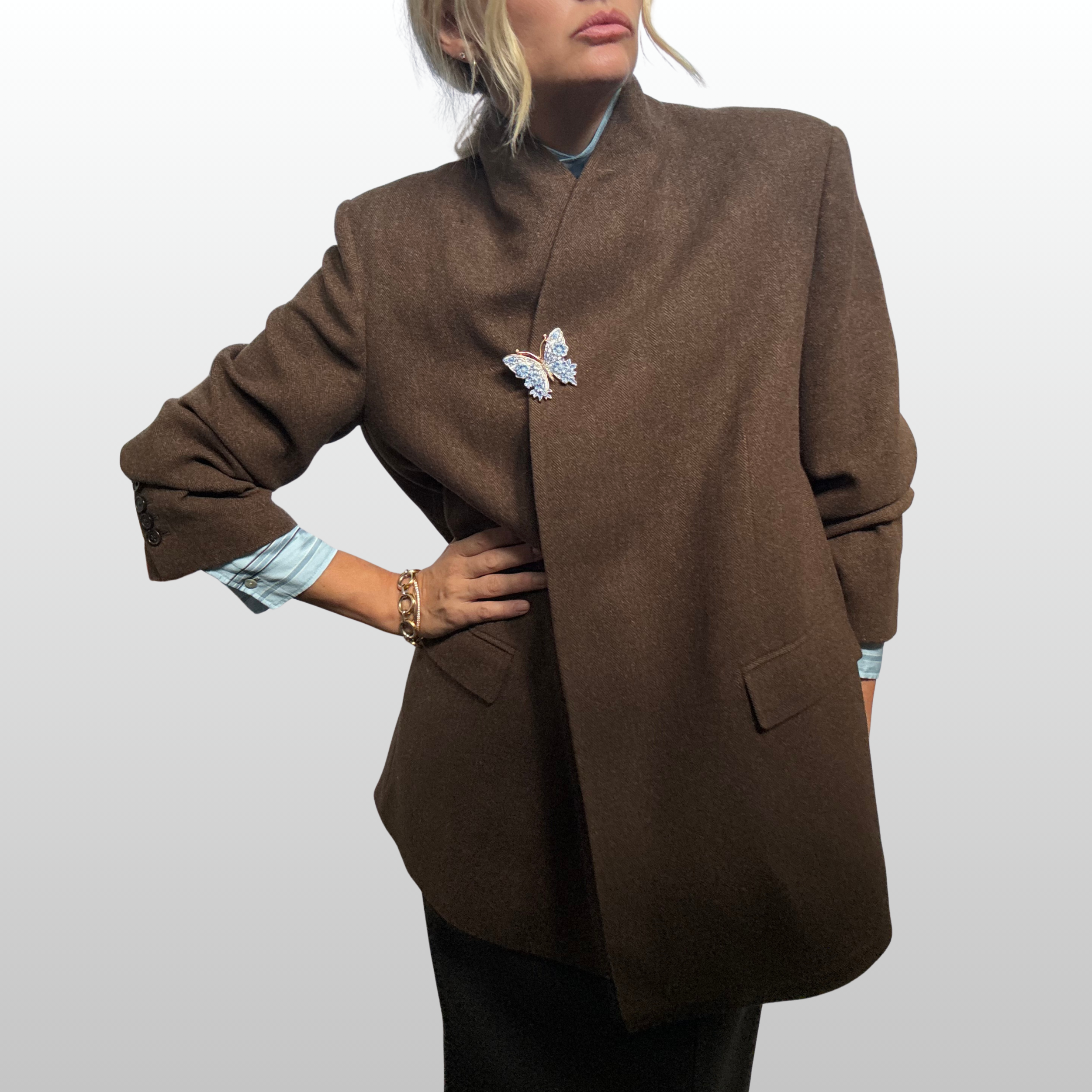 Woman wearing brown blazer with the traditional front button closure replaced by a blue and white butterfly brooch.